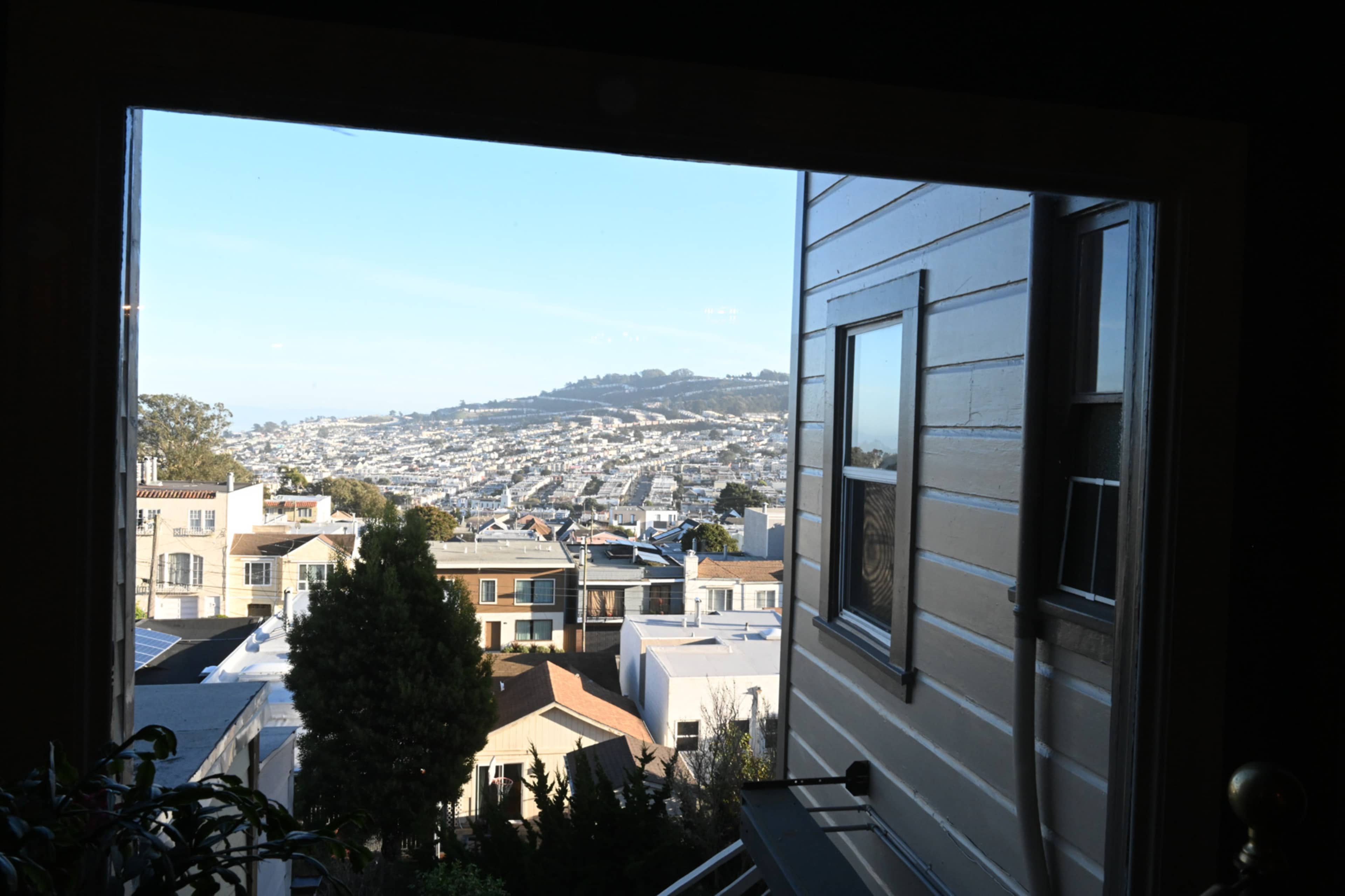 A view from a window overlooking a hilly urban landscape with rows of houses and distant hills.