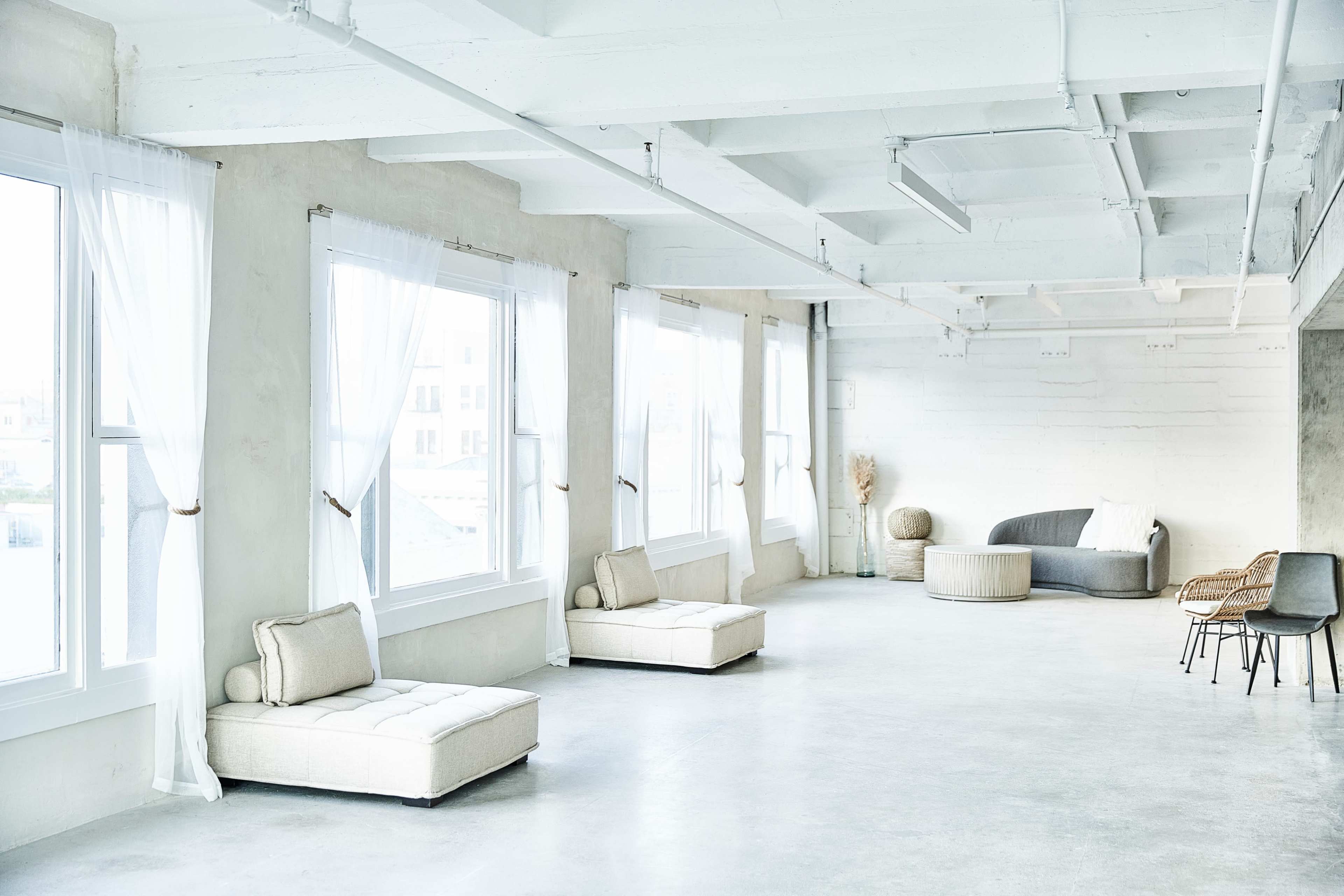 A spacious, well-lit room with large windows, minimalist furniture, and a neutral color palette.