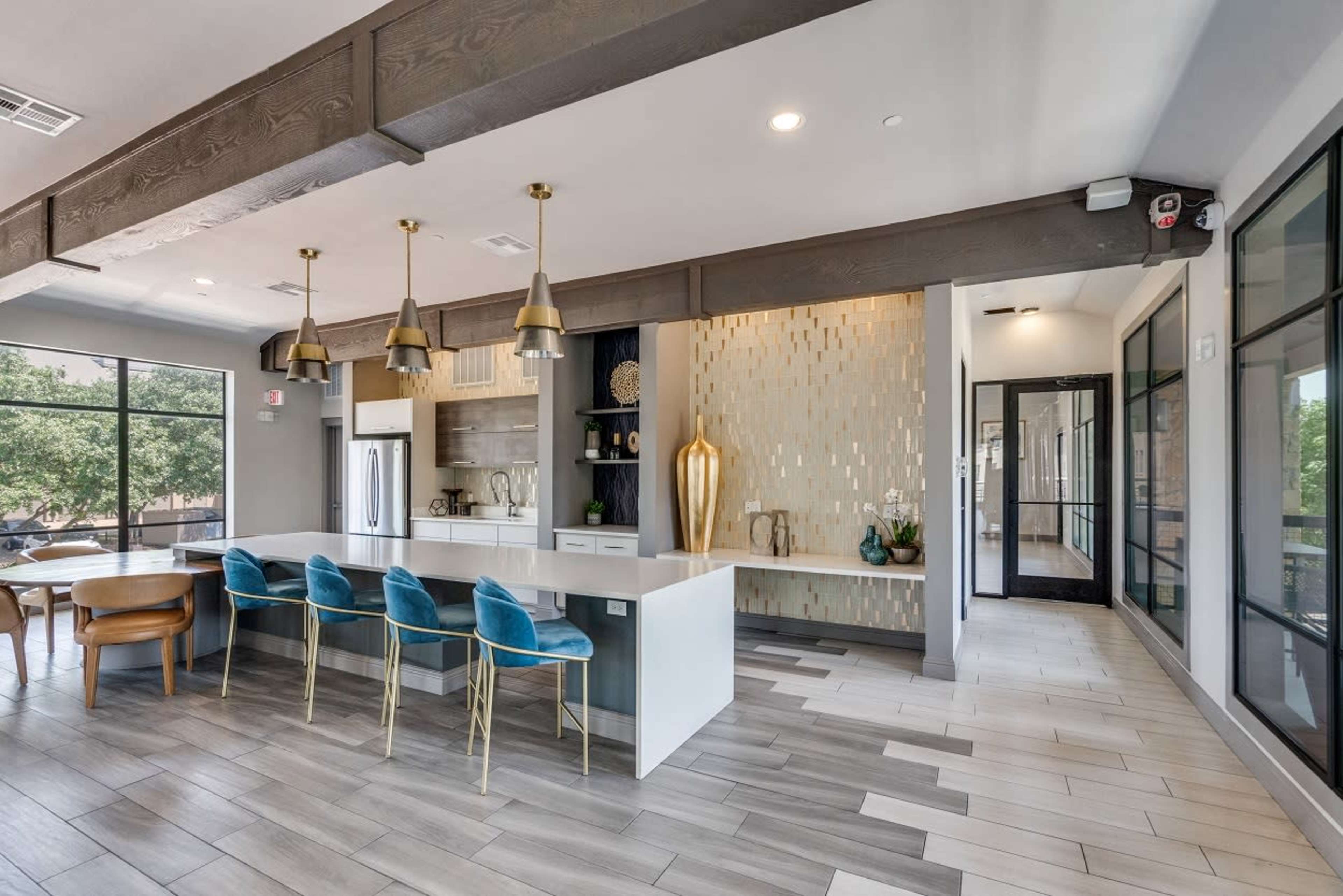 A modern kitchen and dining area featuring a white island countertop, blue upholstered chairs, and a decorative gold vase against a tiled wall.
