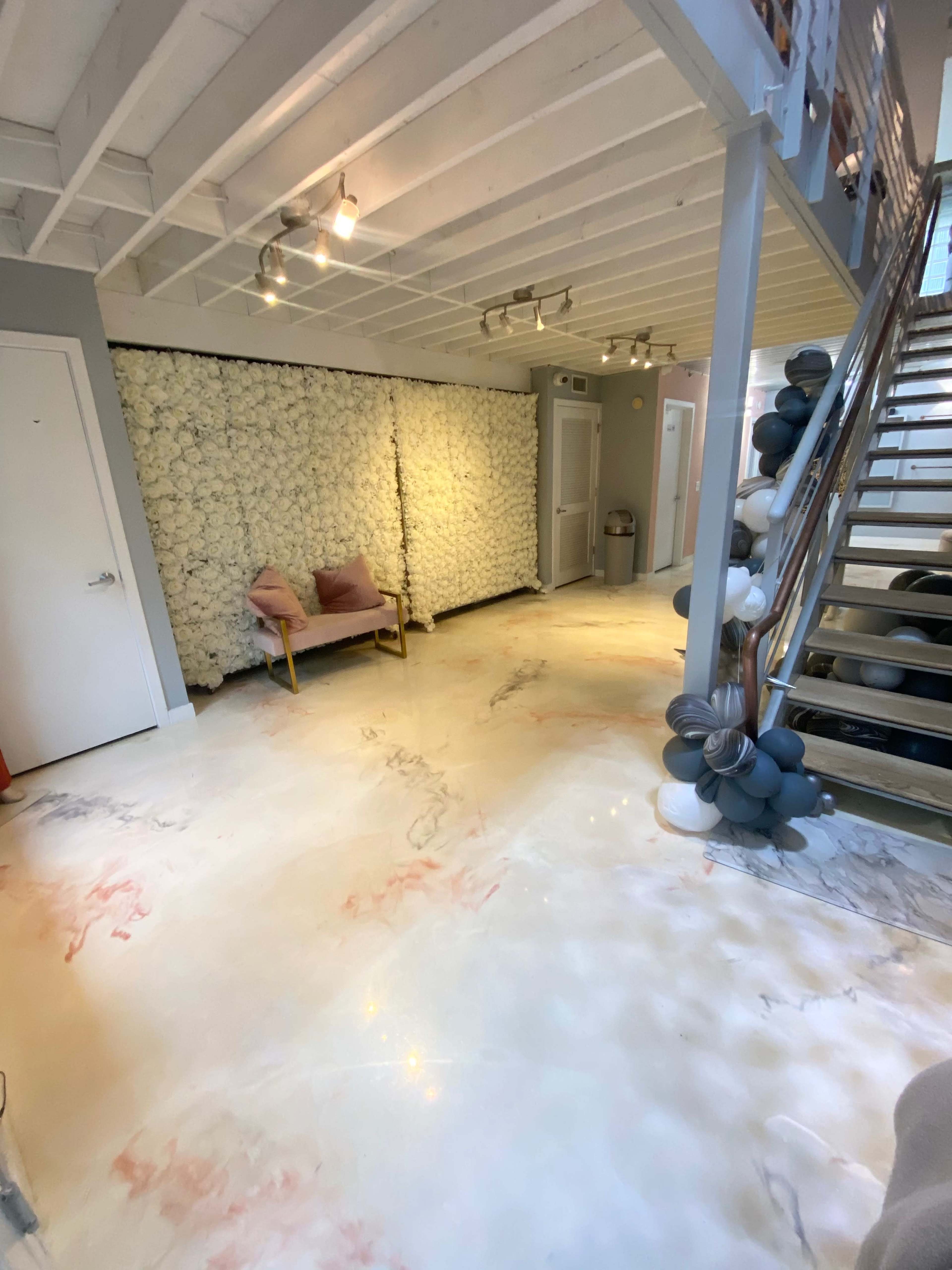 A bright hallway with a floral wallpaper accent wall, a small pink seating area, and a staircase adorned with balloons.