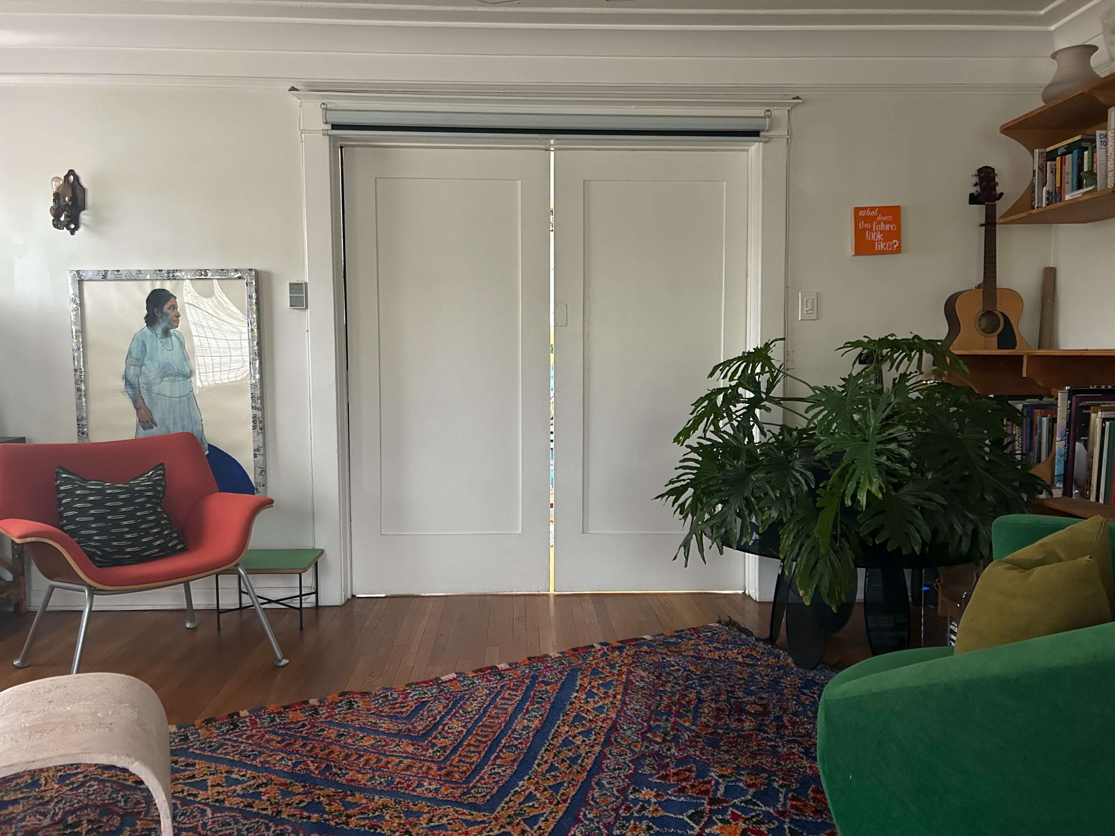 The image shows a living room with two closed sliding doors, a large plant, a colorful rug, and various pieces of furniture including chairs and a guitar in the background.