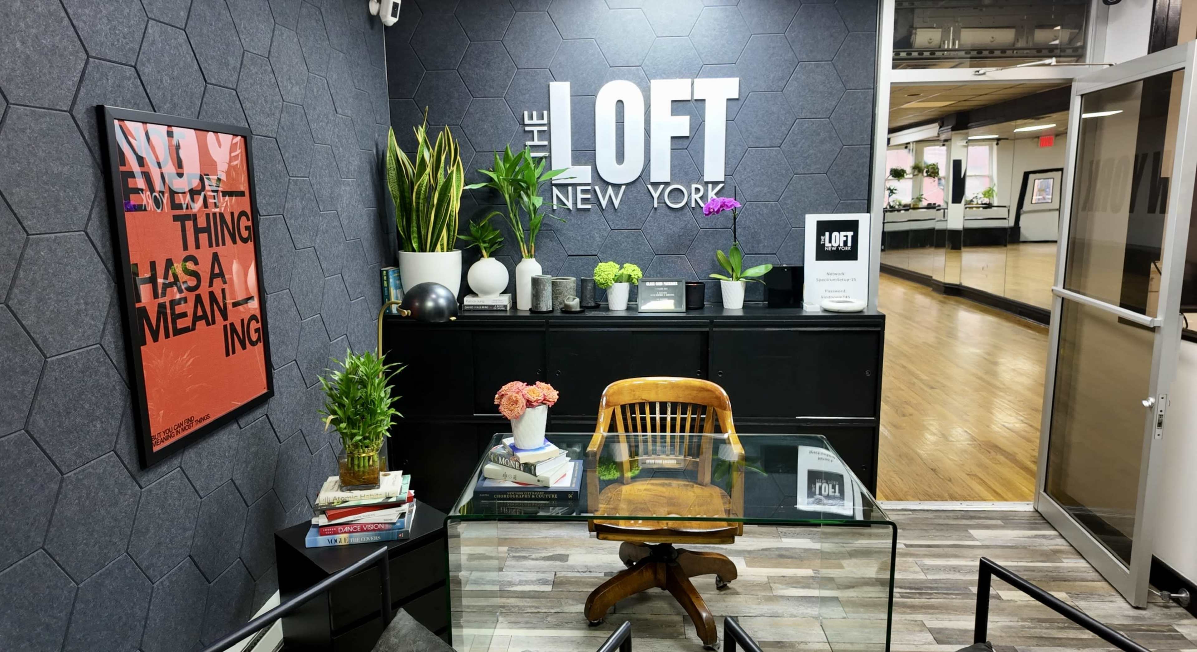 The image shows a modern reception area labeled "The Loft New York," featuring plants, artwork, and a glass table with a wooden chair.