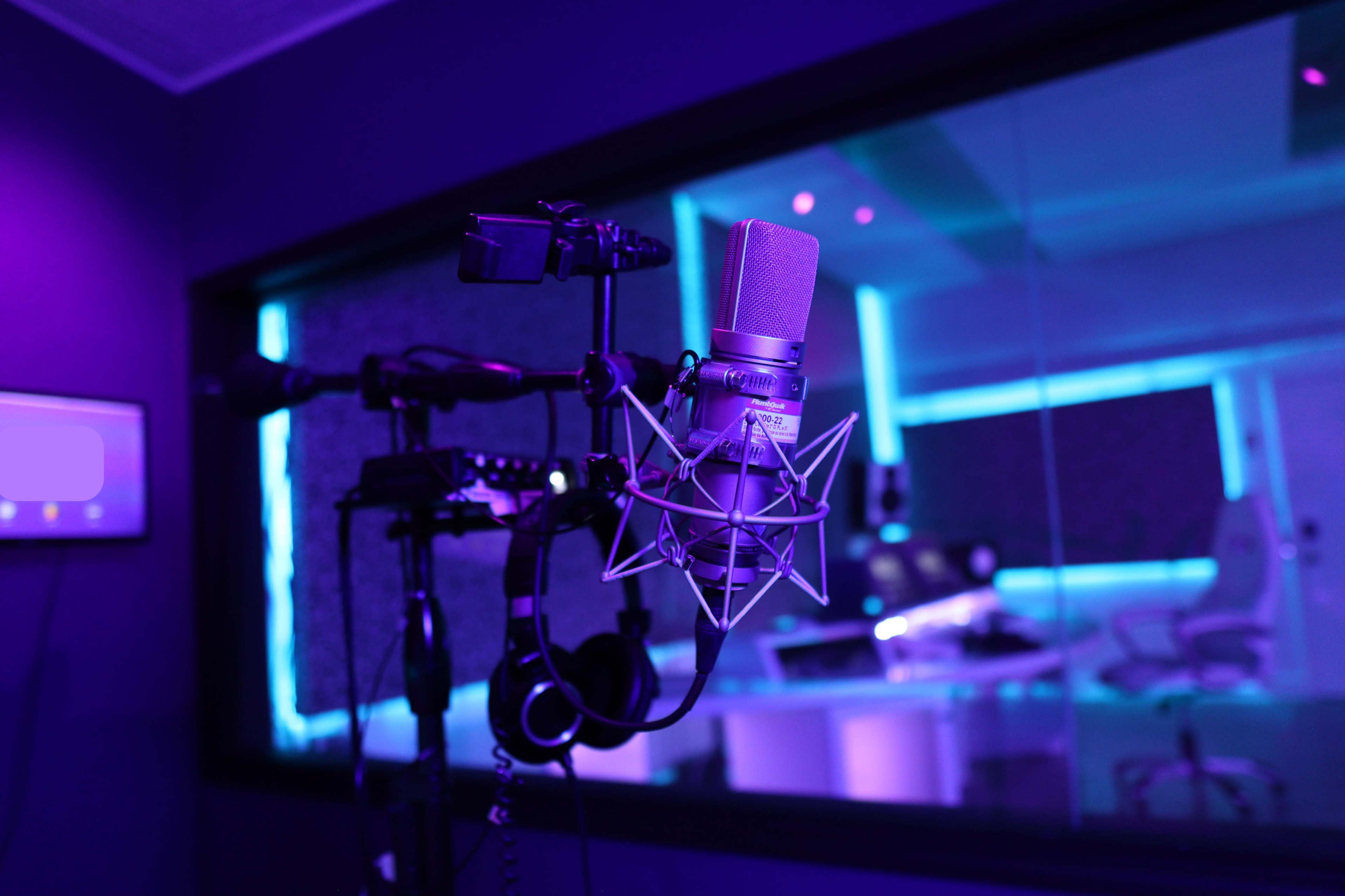 A professional studio microphone is mounted on a stand in a dimly lit recording studio with blue and purple lighting.