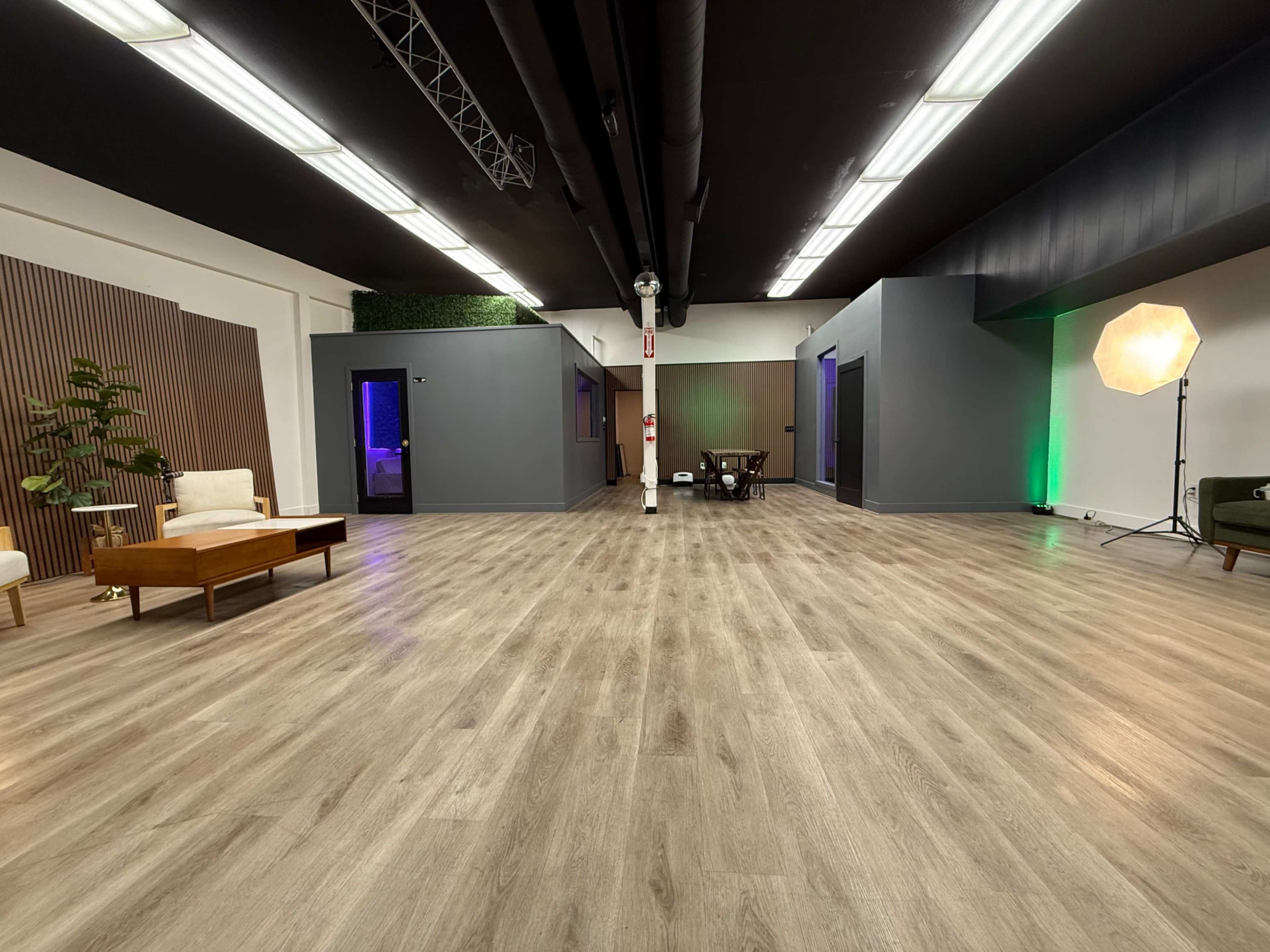 The image shows a spacious, empty interior with wooden flooring, several rooms divided by gray walls, and a few pieces of furniture, including a sofa and a table.