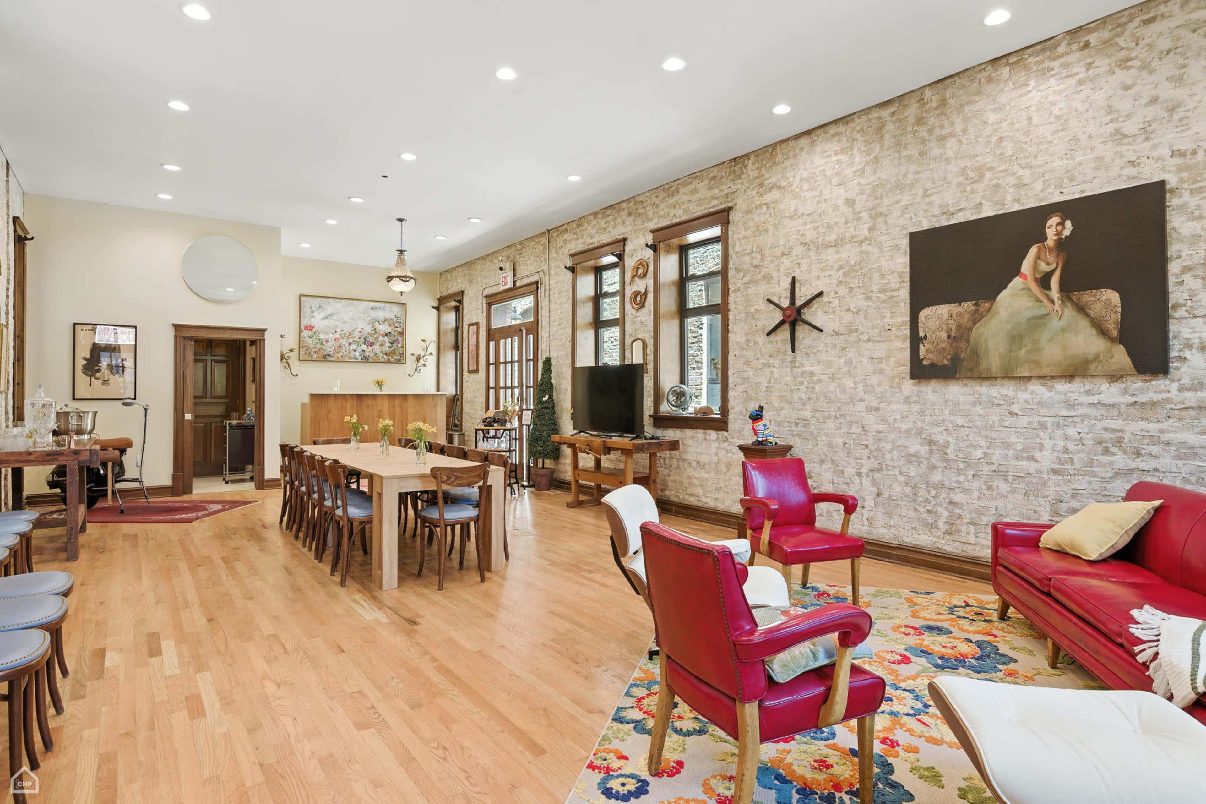 The spacious living area features hardwood floors, exposed brick walls, a dining table, and a mix of modern and eclectic furniture.