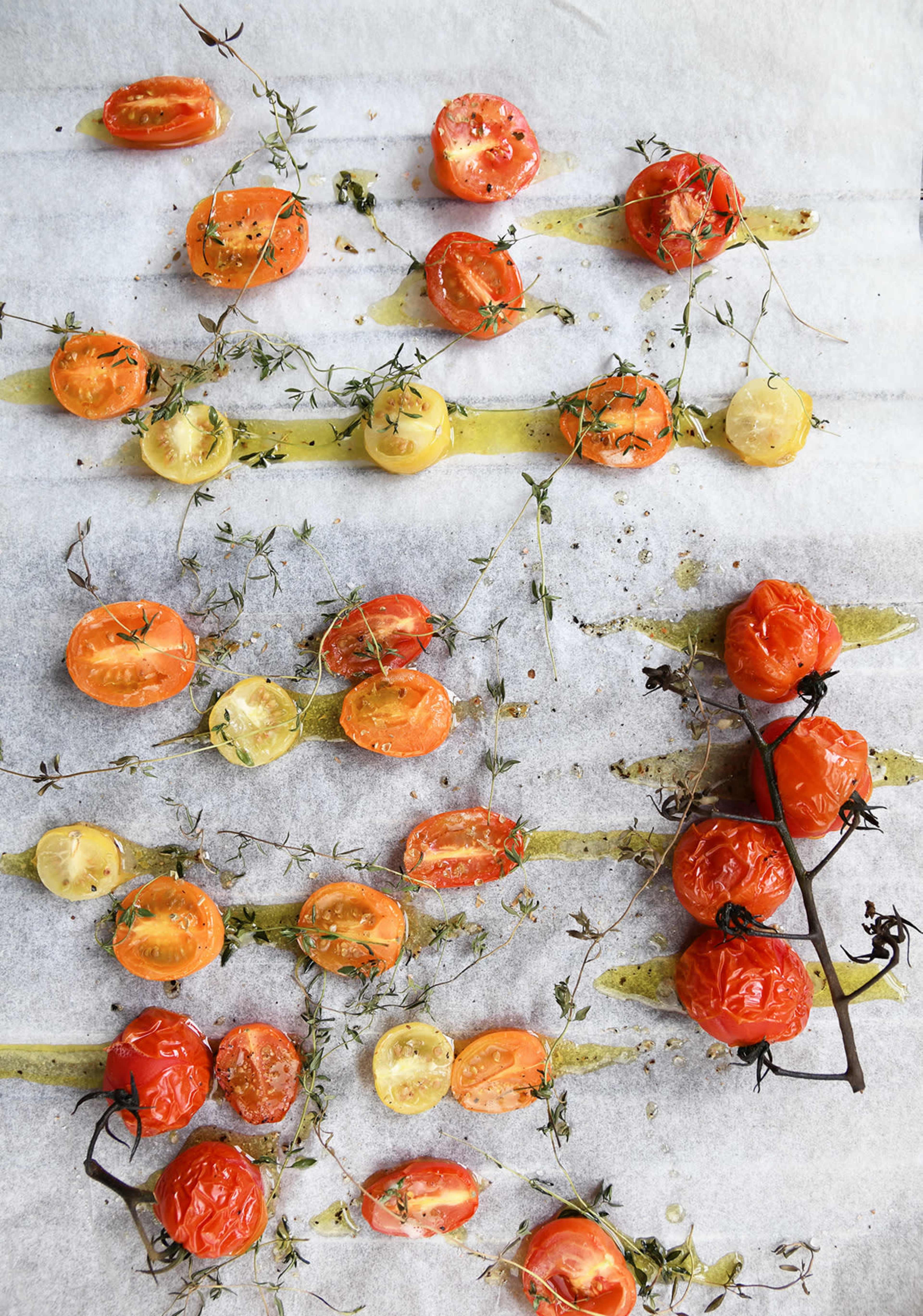 Halved tomatoes and sprigs of thyme arranged on a baking sheet with drizzled olive oil.