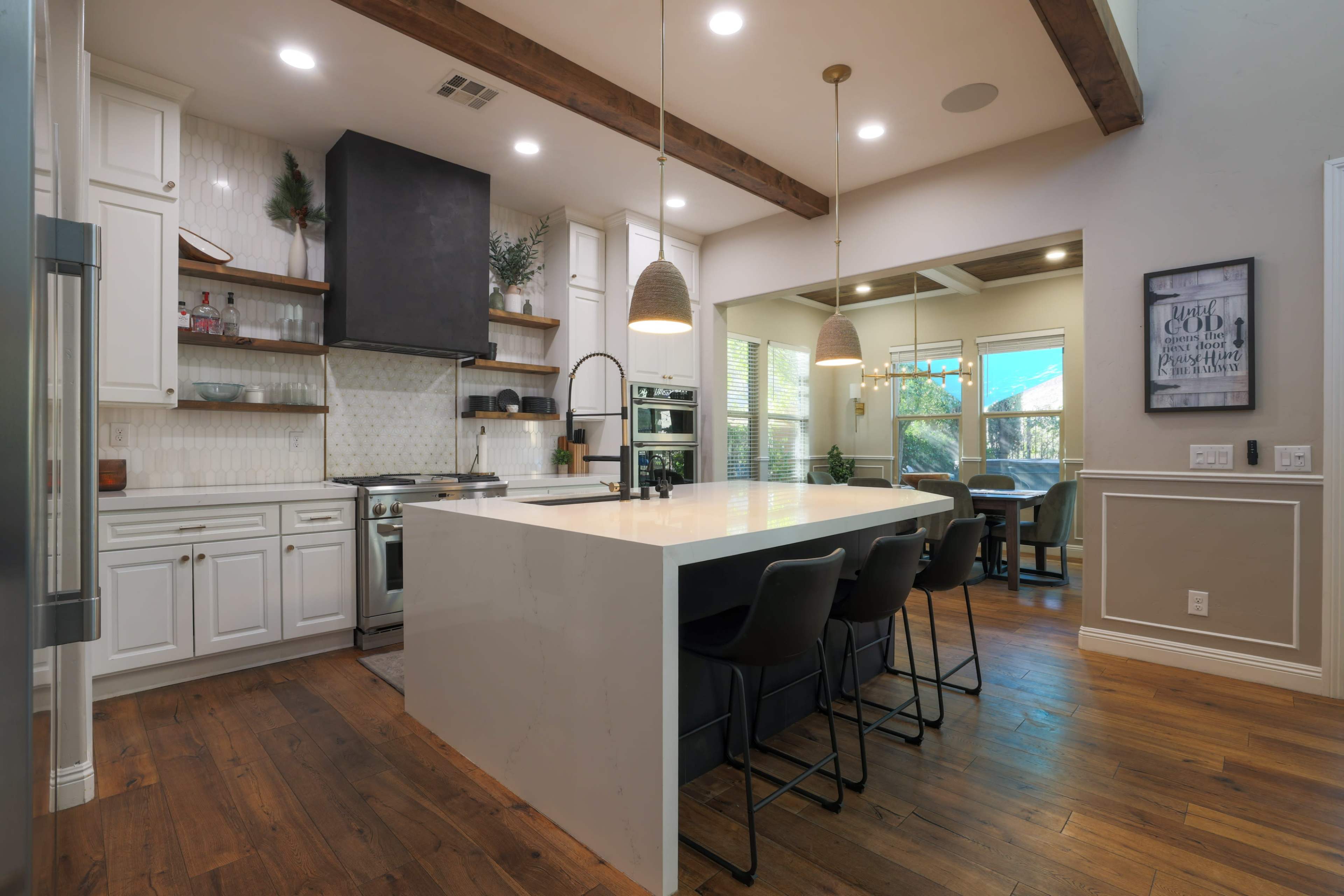 The image shows a modern kitchen with a large island, white cabinetry, and wood beams on the ceiling.
