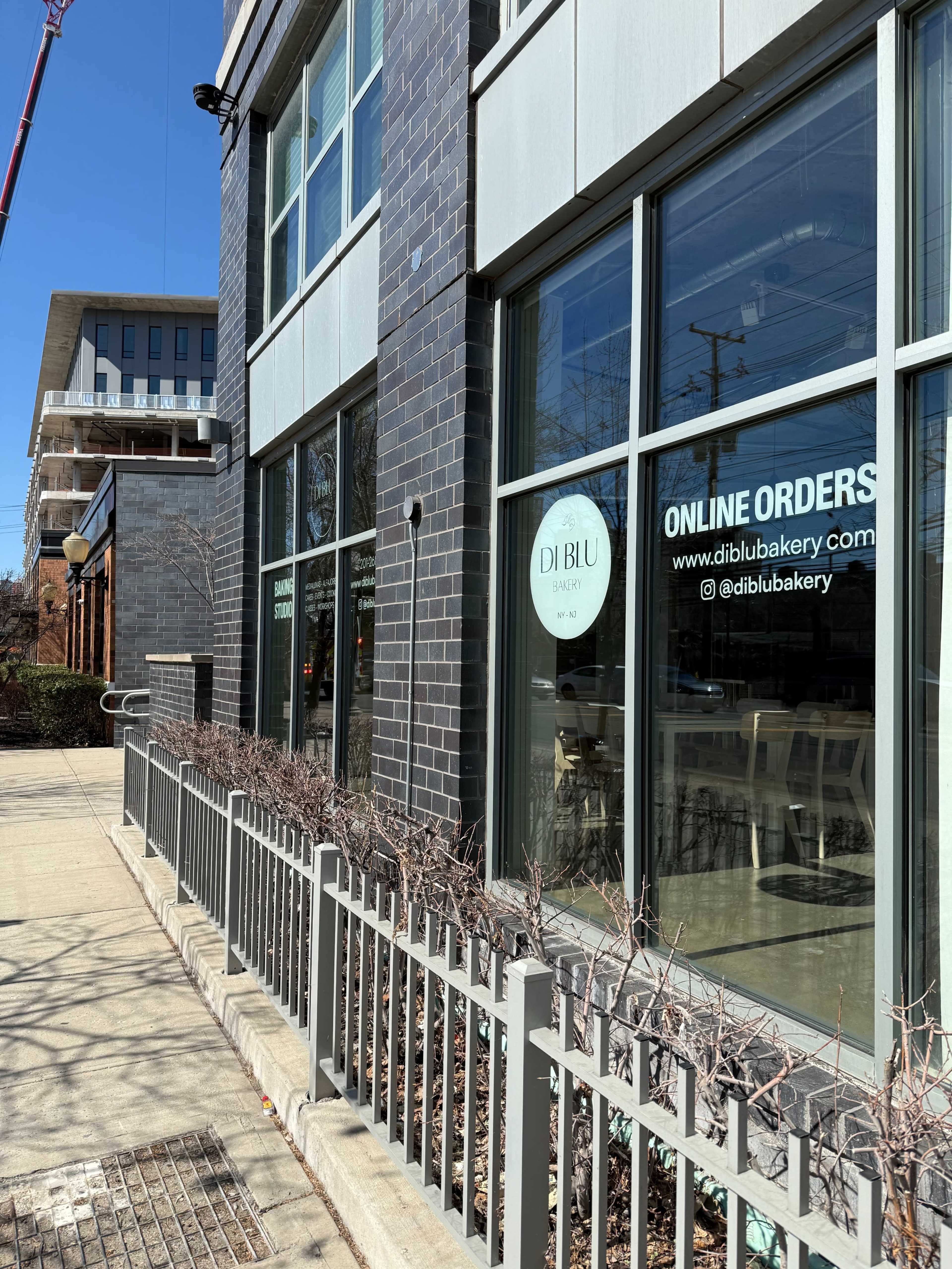 The image shows a gray brick building with large windows displaying the "DI BLU" bakery and an "ONLINE ORDERS" sign.