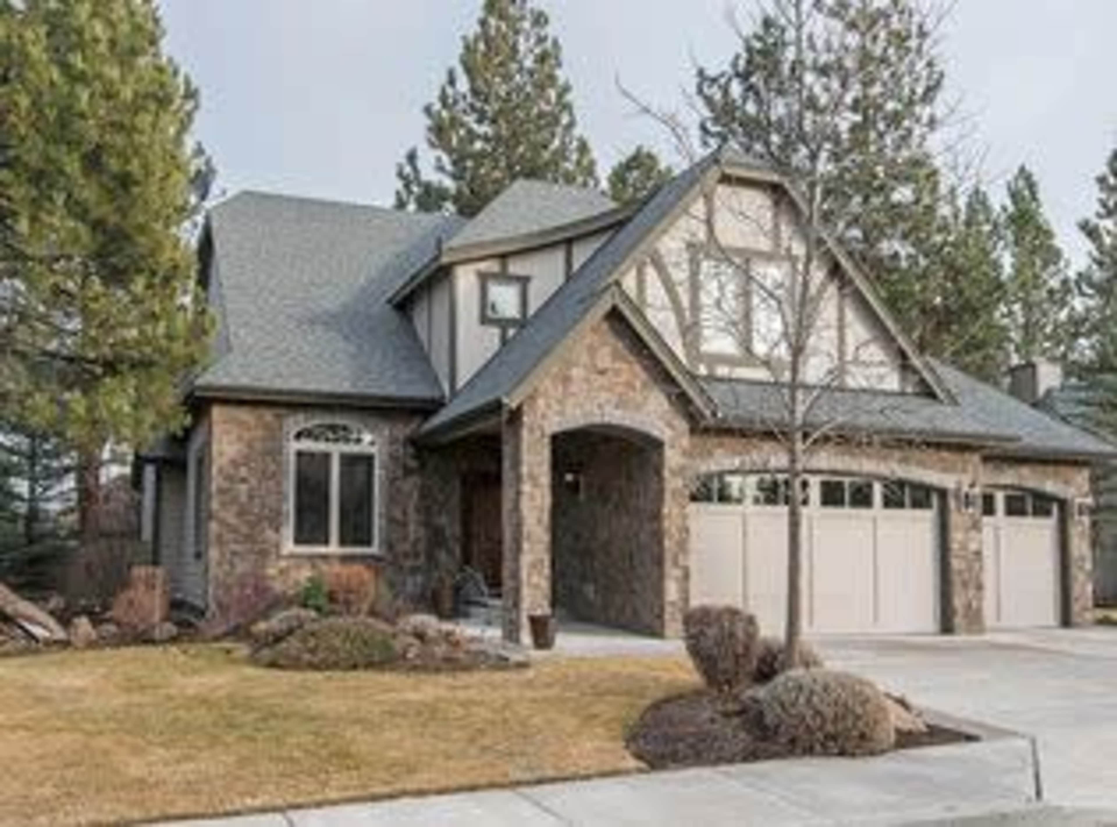 A large two-story house with a stone exterior, a gray roof, and a landscaped front yard.