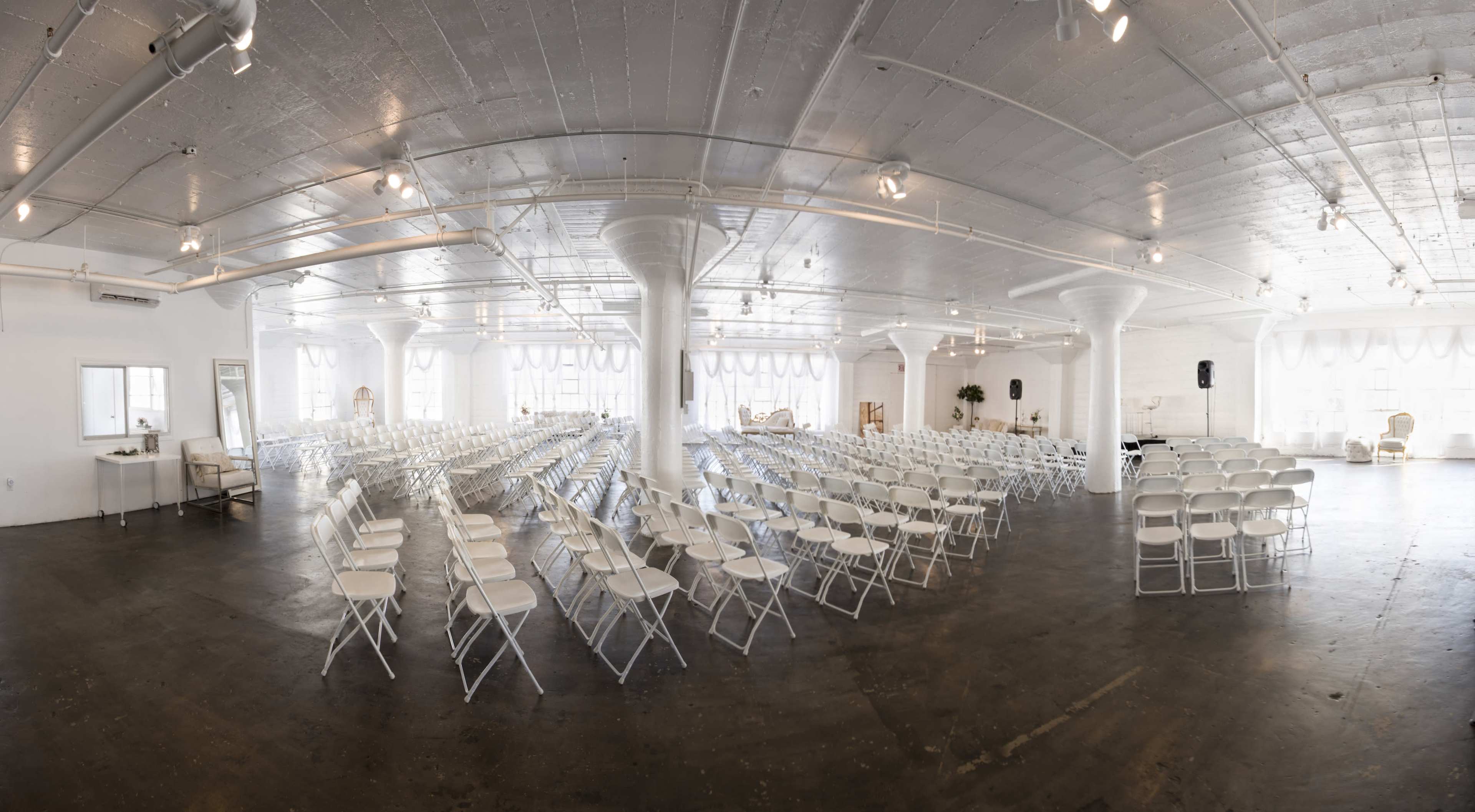 A large, empty event space set up with rows of white folding chairs arranged for an event.