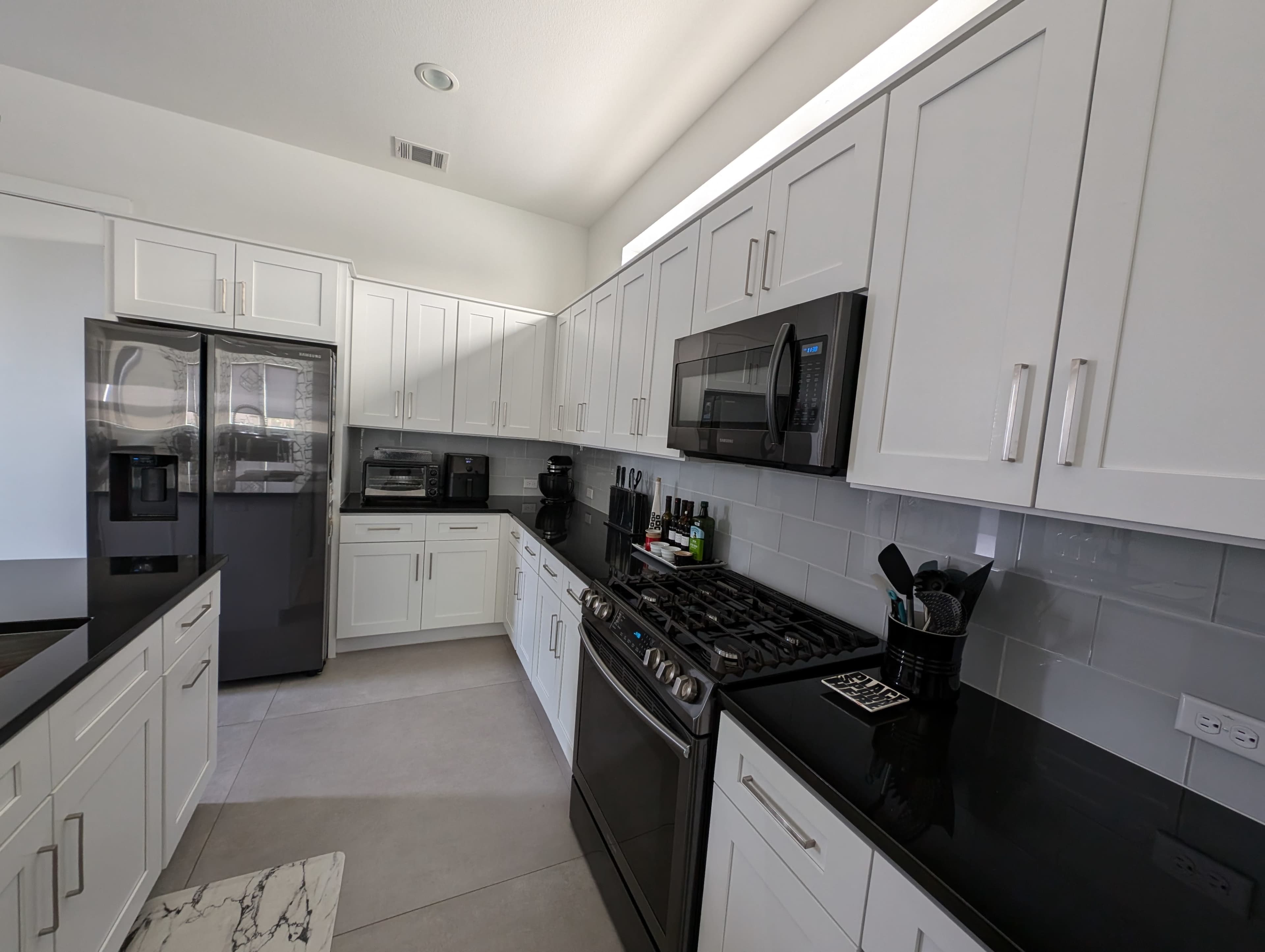 A modern kitchen with white cabinets, black countertops, and stainless steel appliances arranged along two walls.
