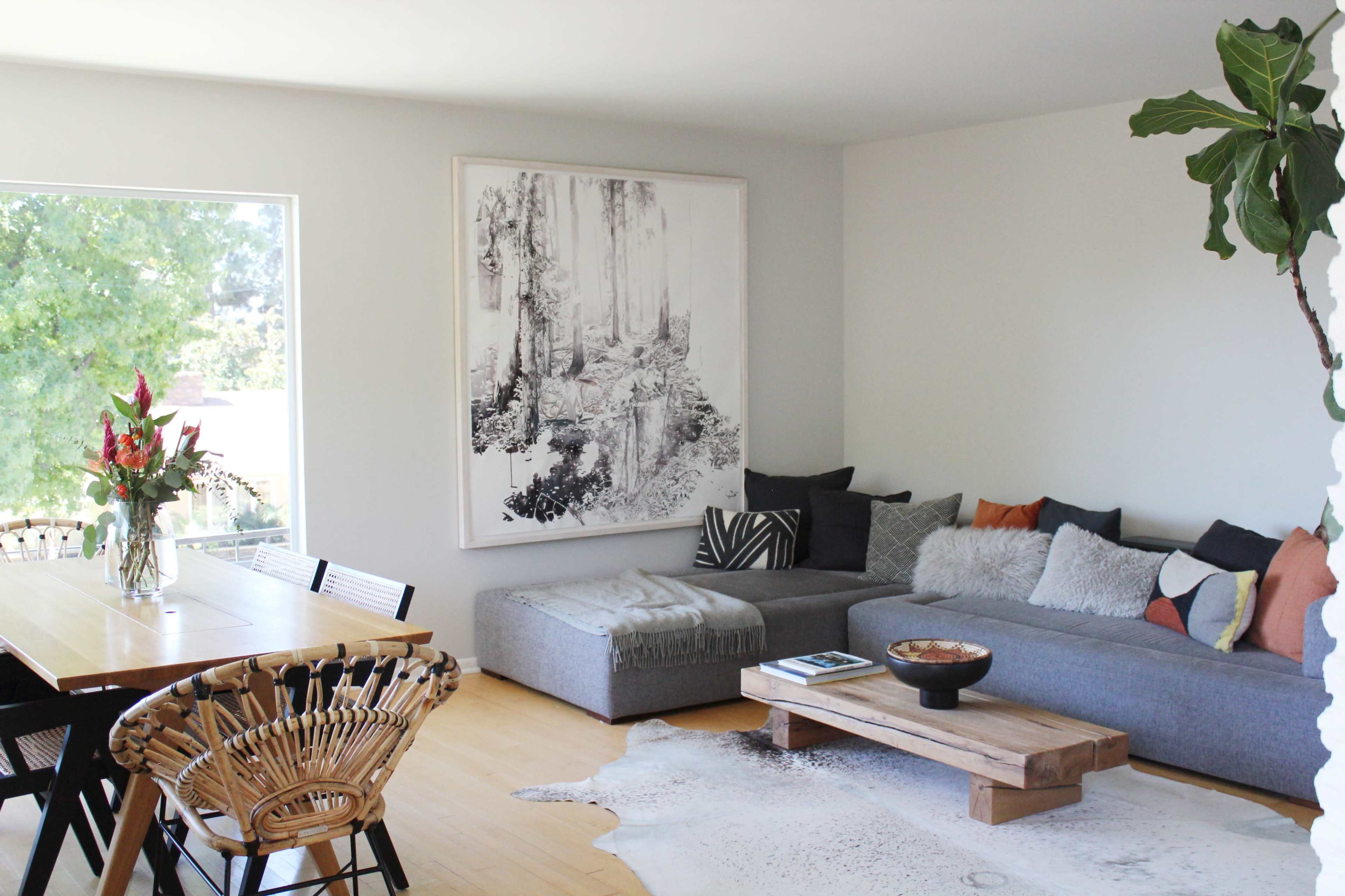 A modern living room features a gray sectional sofa, a wooden coffee table, and a dining area with a long table surrounded by black chairs and a rattan chair.