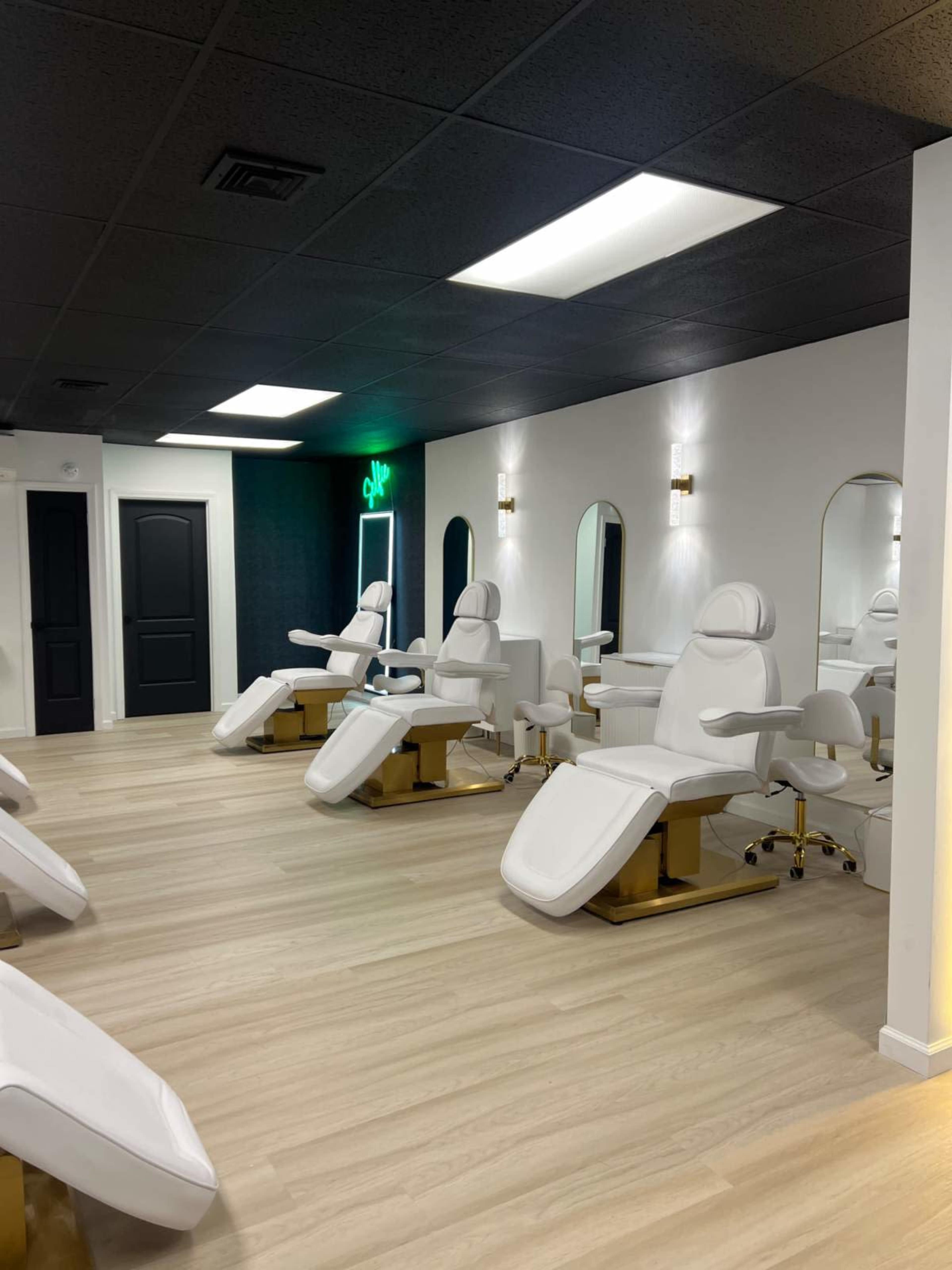 A modern beauty salon interior with several white treatment chairs and golden accents, illuminated by overhead lighting.