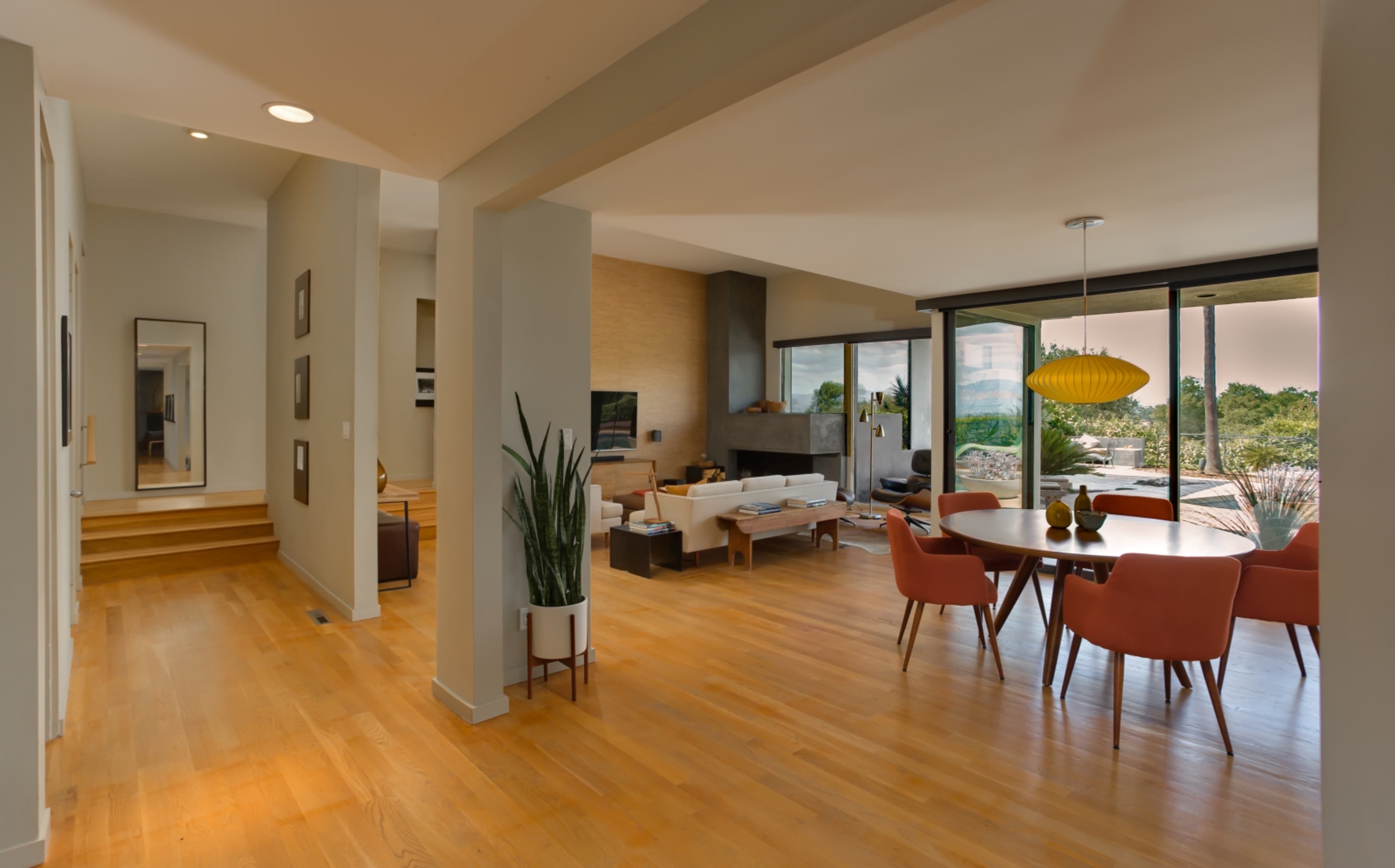 A modern living space featuring an open floor plan with a dining area, living area, large windows, and wooden flooring.