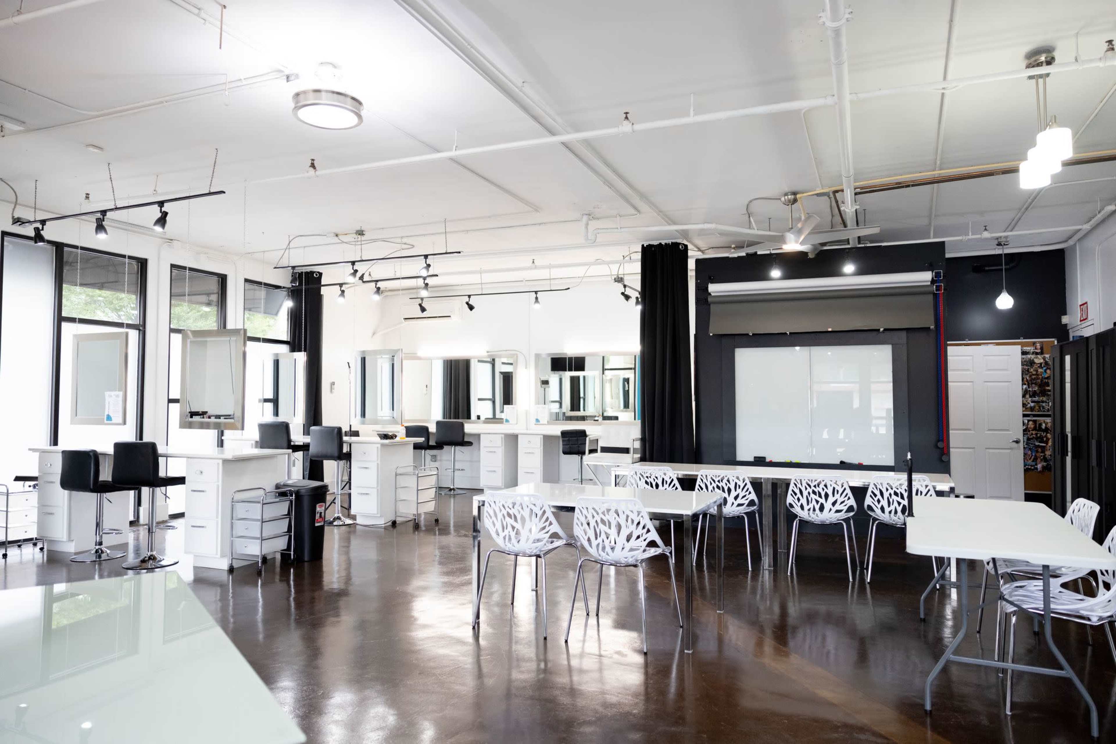 A spacious, modern studio with multiple workstations, white tables, and clear plastic chairs arranged in an open layout.