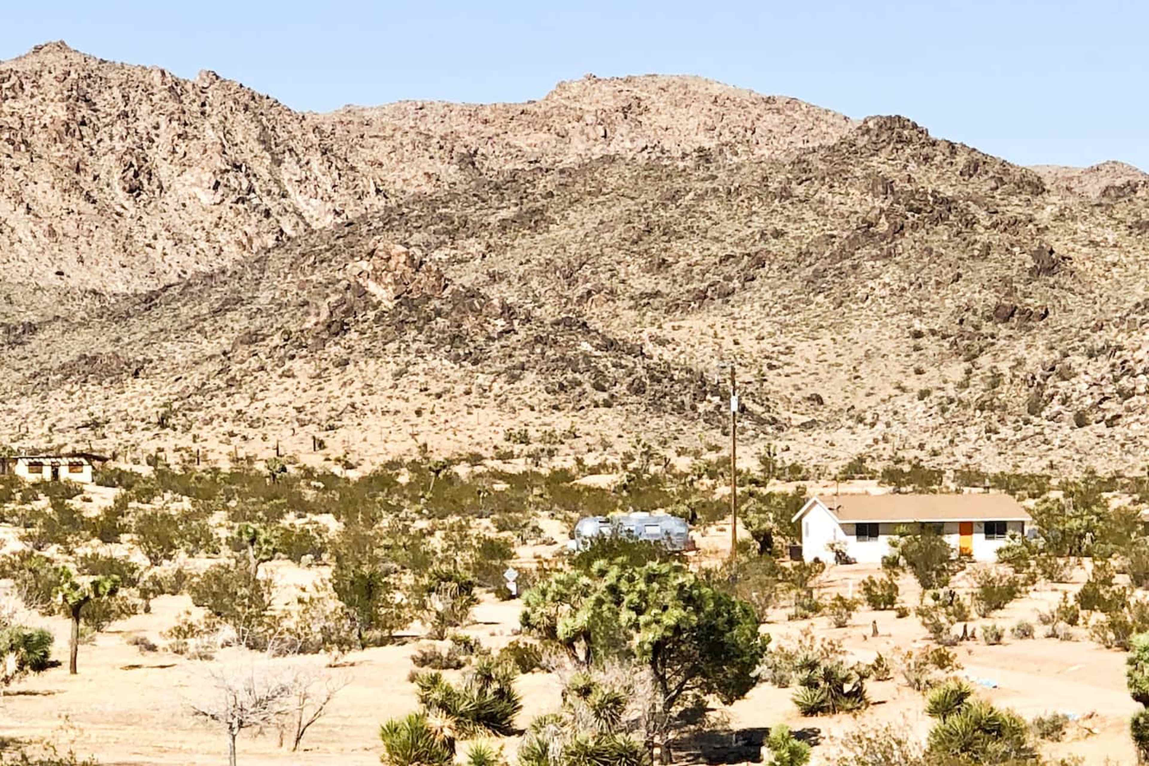 A small house situated in a desert landscape, surrounded by sparse vegetation and mountains in the background.