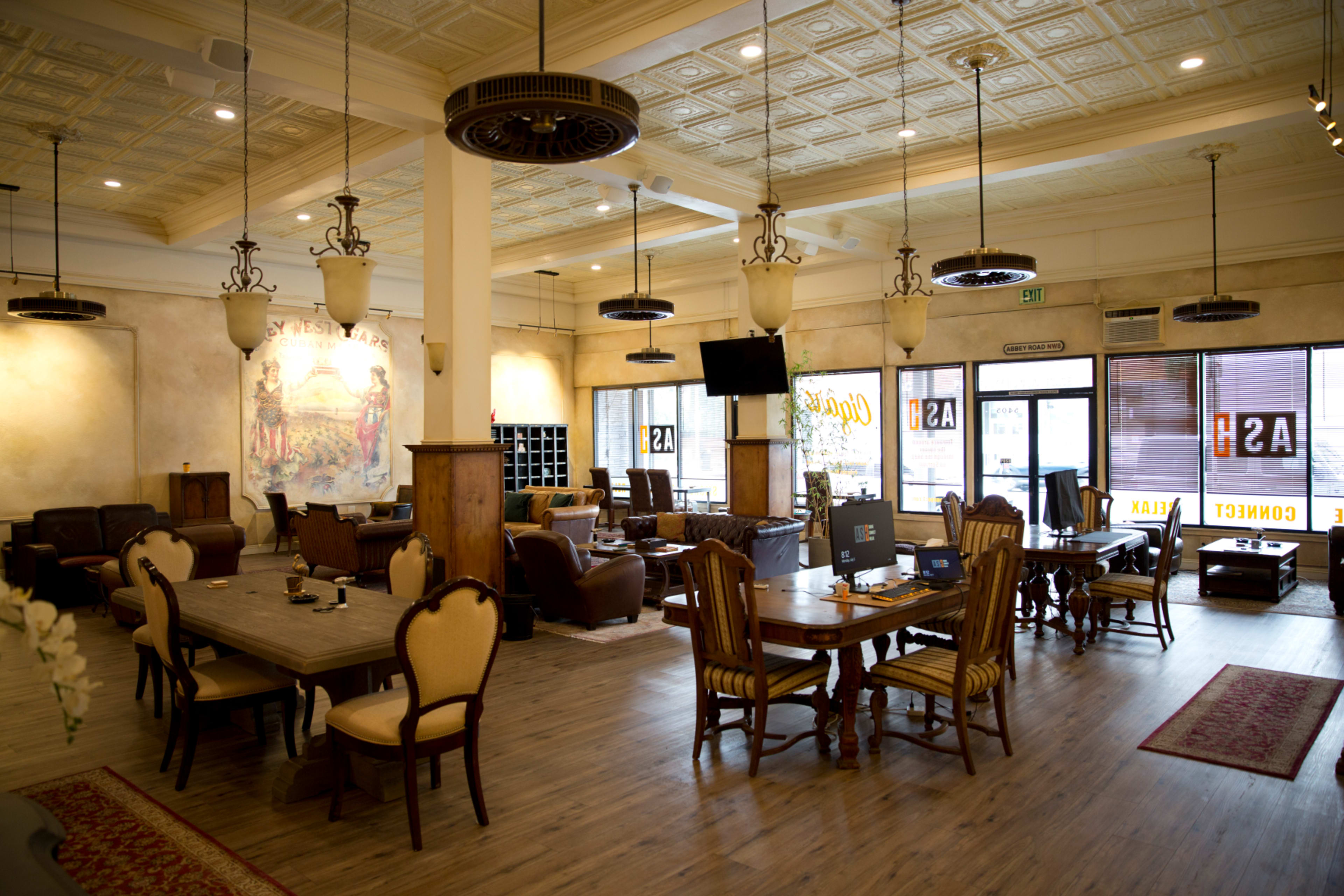 A spacious lounge with wooden tables, leather chairs, decorative ceiling tiles, and a mural on the wall.