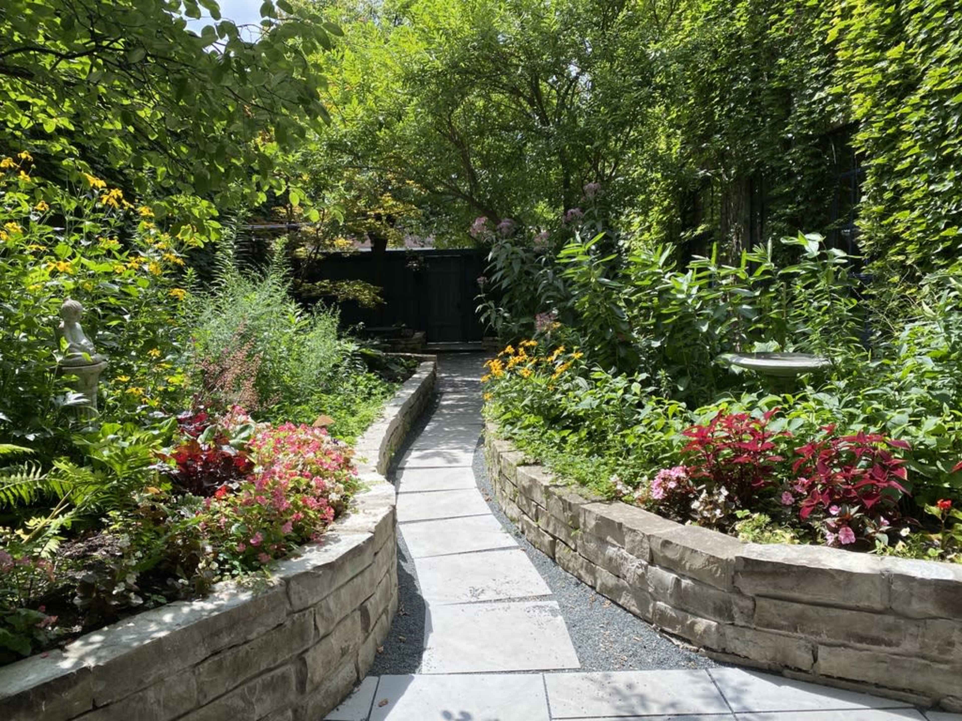 A stone pathway curves through a lush garden filled with colorful flowers and greenery.