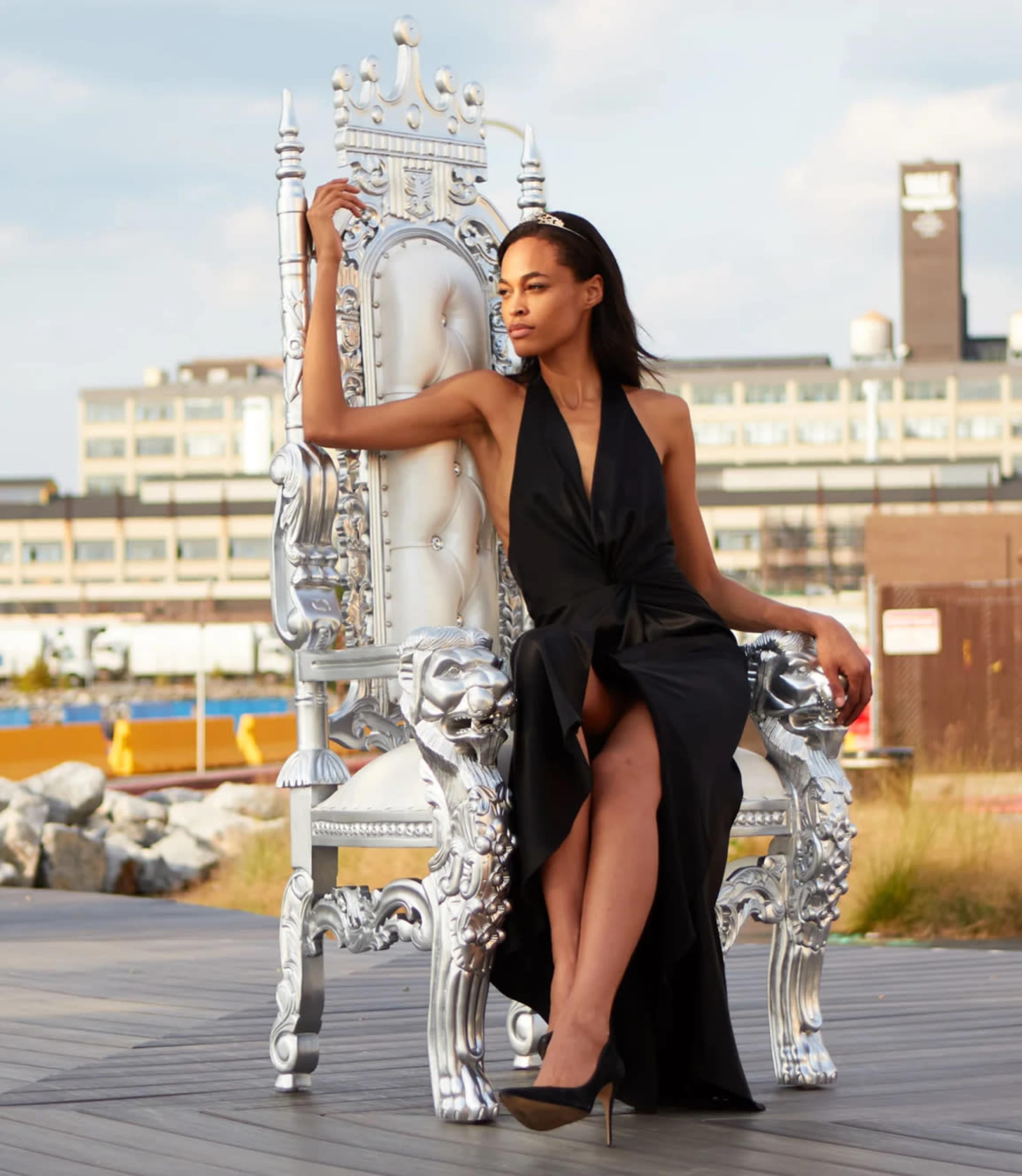 A woman in a black gown sits elegantly on a large silver throne.