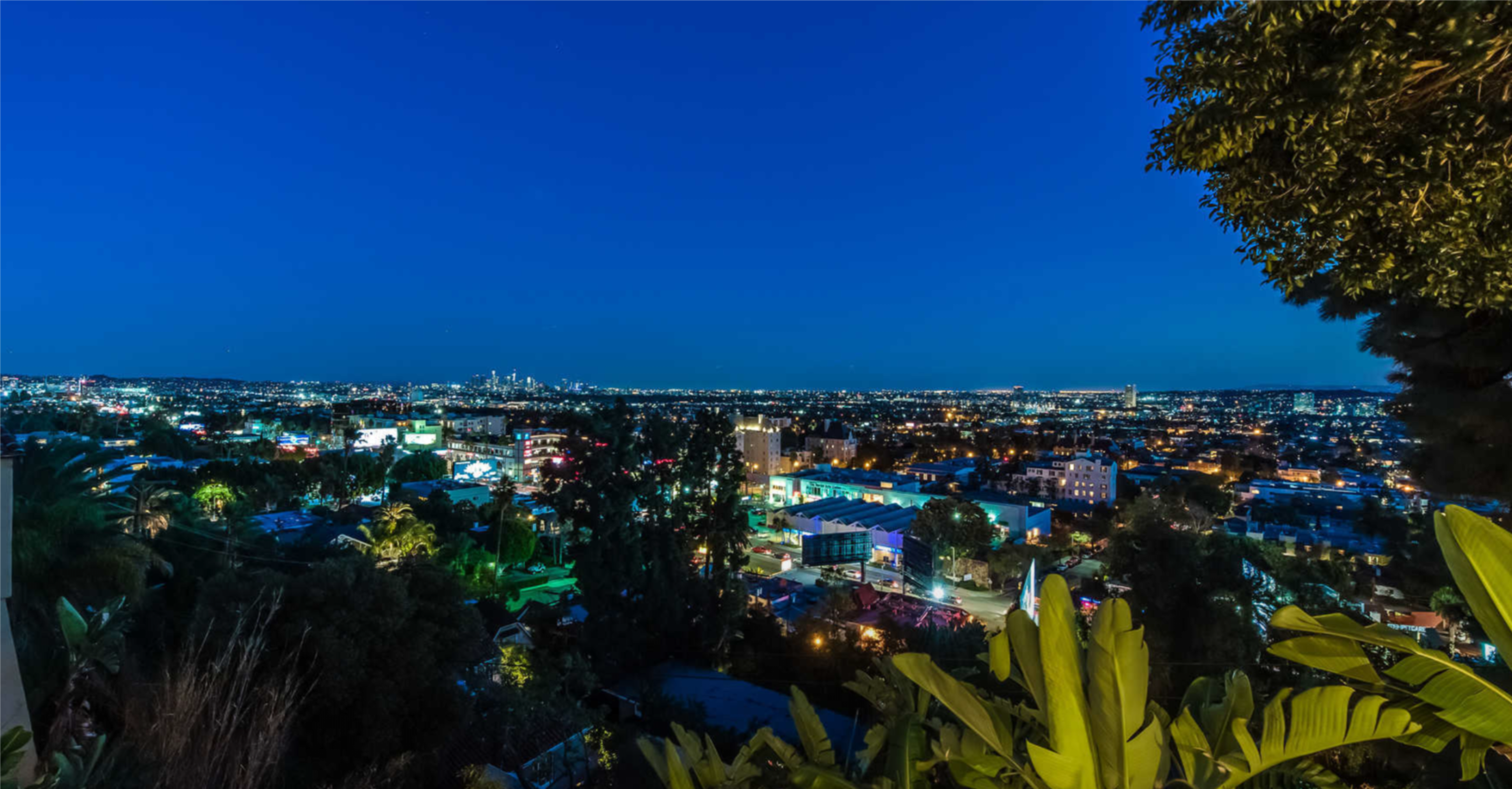 A panoramic view of a city skyline at night, illuminated by various lights against a deep blue sky.