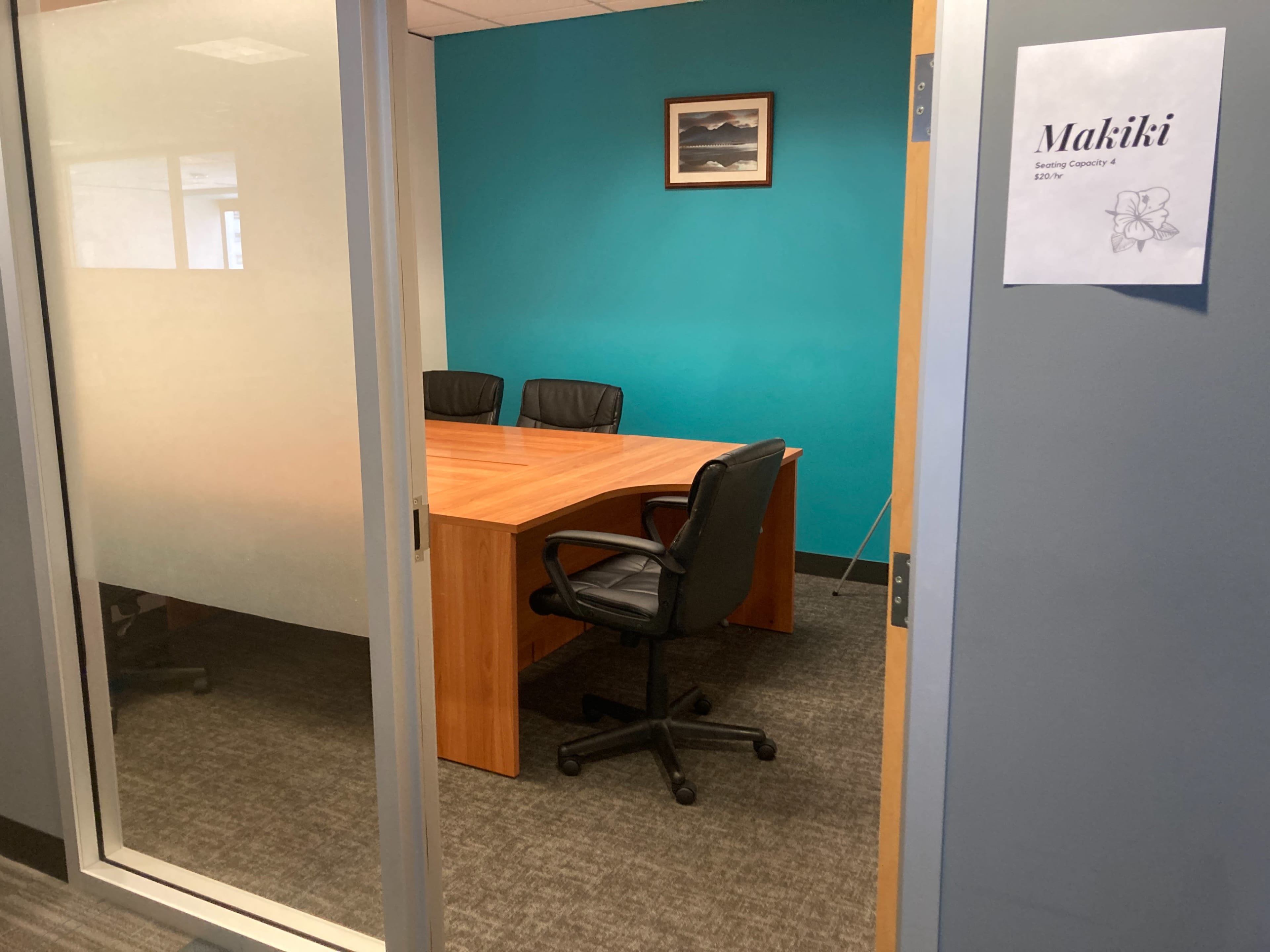 A small conference room with a wooden table and four black chairs, surrounded by blue and gray walls.