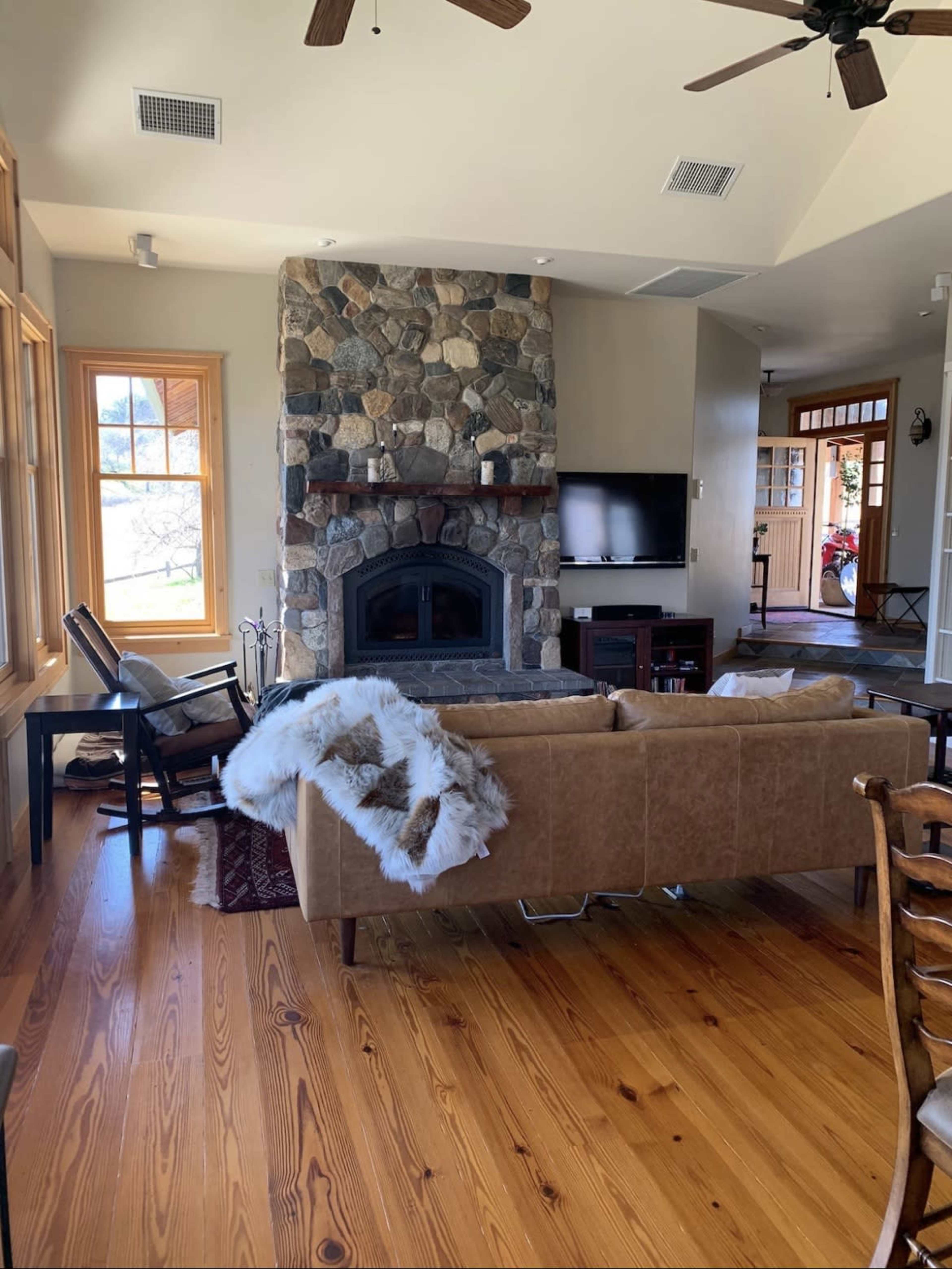 A cozy living room with a stone fireplace, a large sofa, hardwood floors, and a view of a front door leading outside.