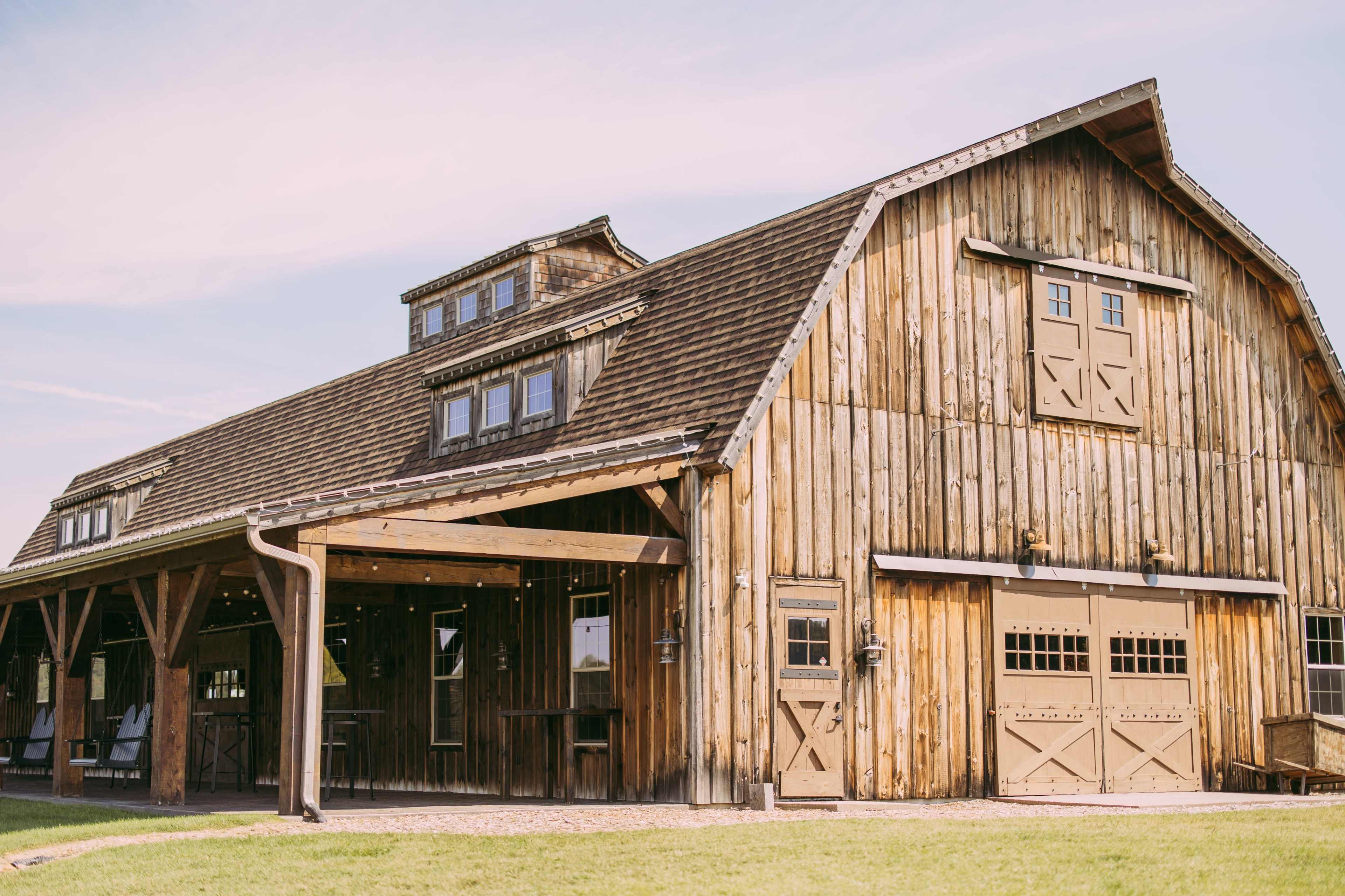 A large wooden barn with multiple windows and a sloped roof sits on a grassy area under a clear sky.