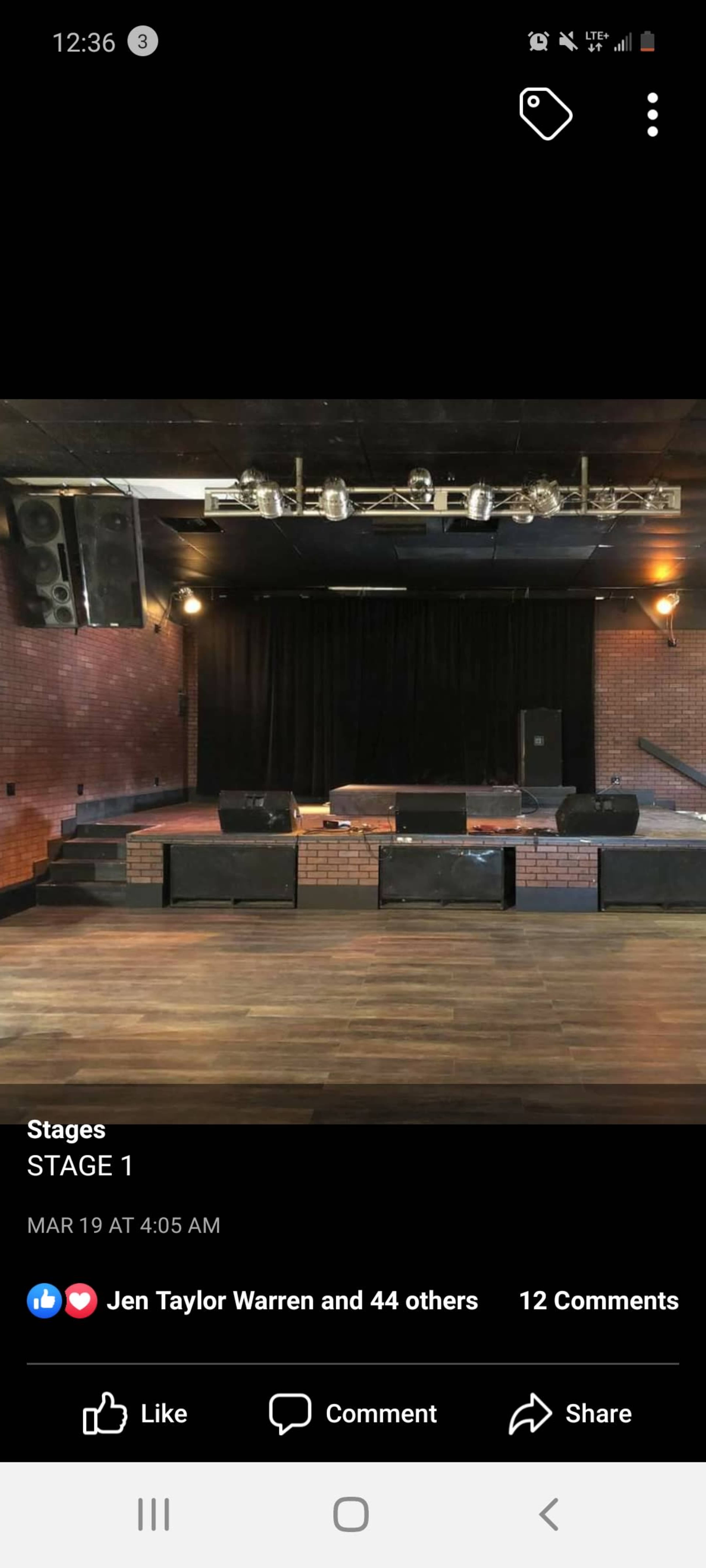 A performance stage with a black curtain backdrop, multiple speakers, and a wooden floor.