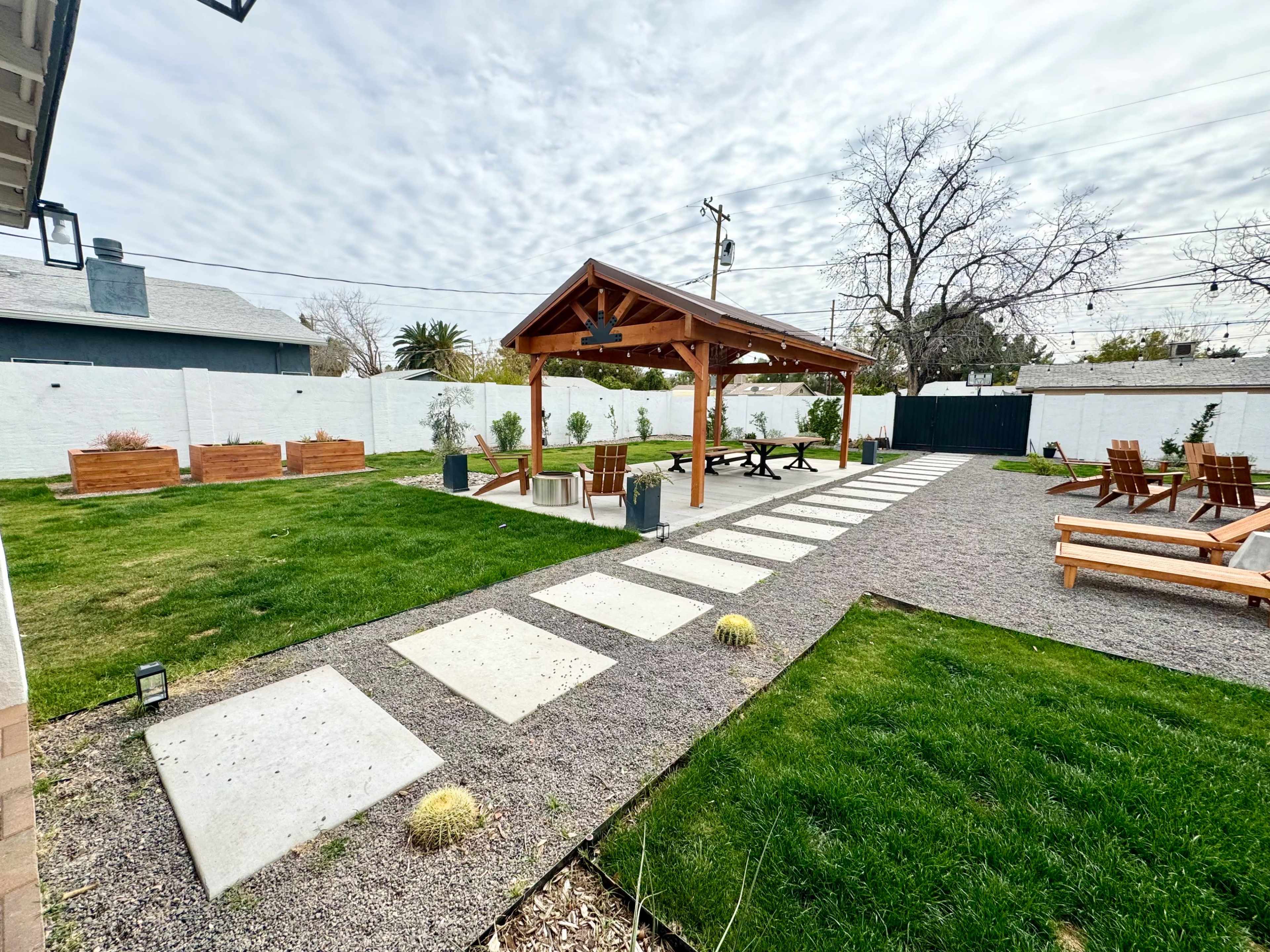 A landscaped outdoor space featuring a wooden pavilion with seating, a gravel pathway, and neatly arranged grass and planters.