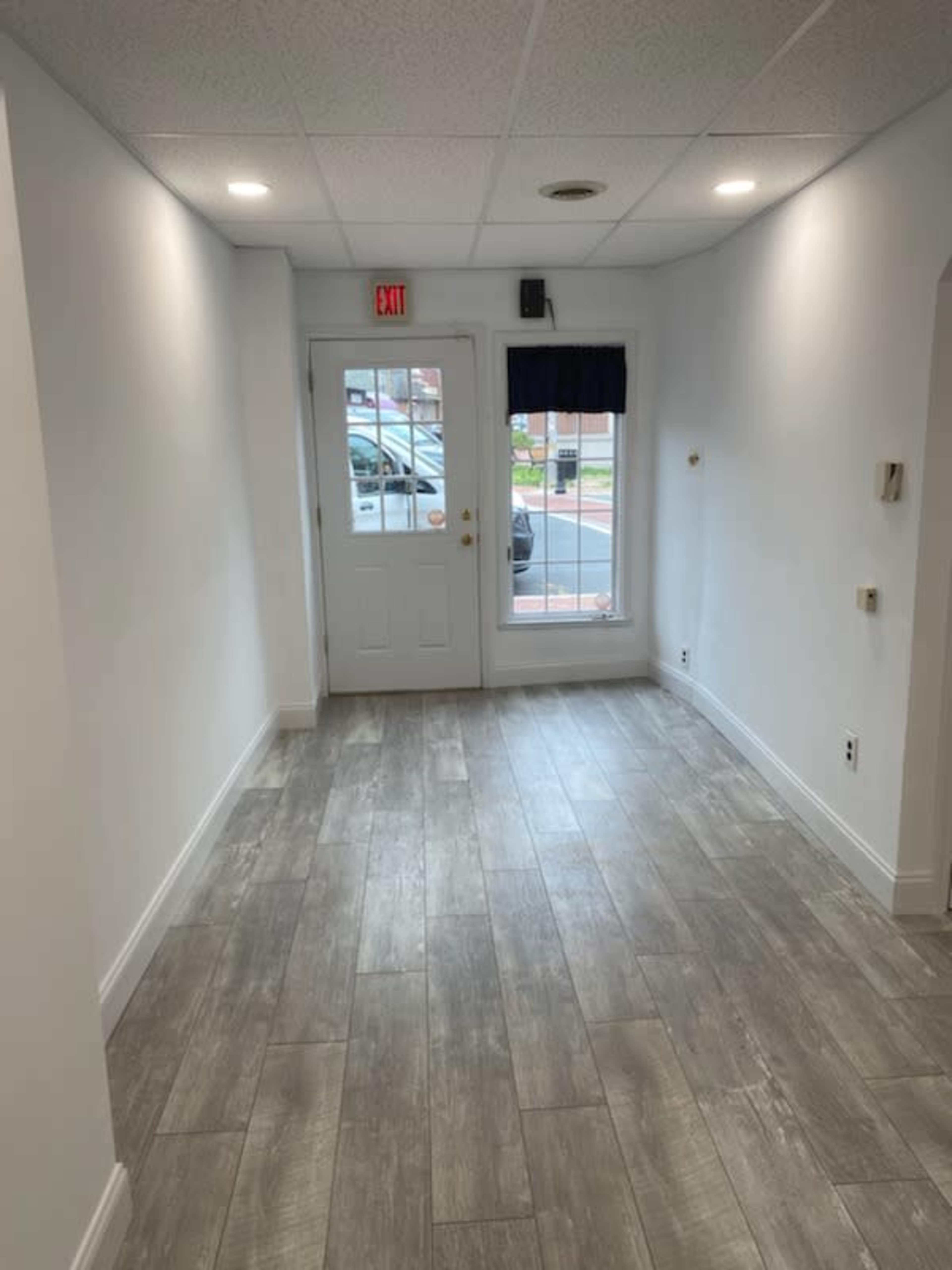A well-lit hallway with light gray tiled floors leading to a door and a window at one end.