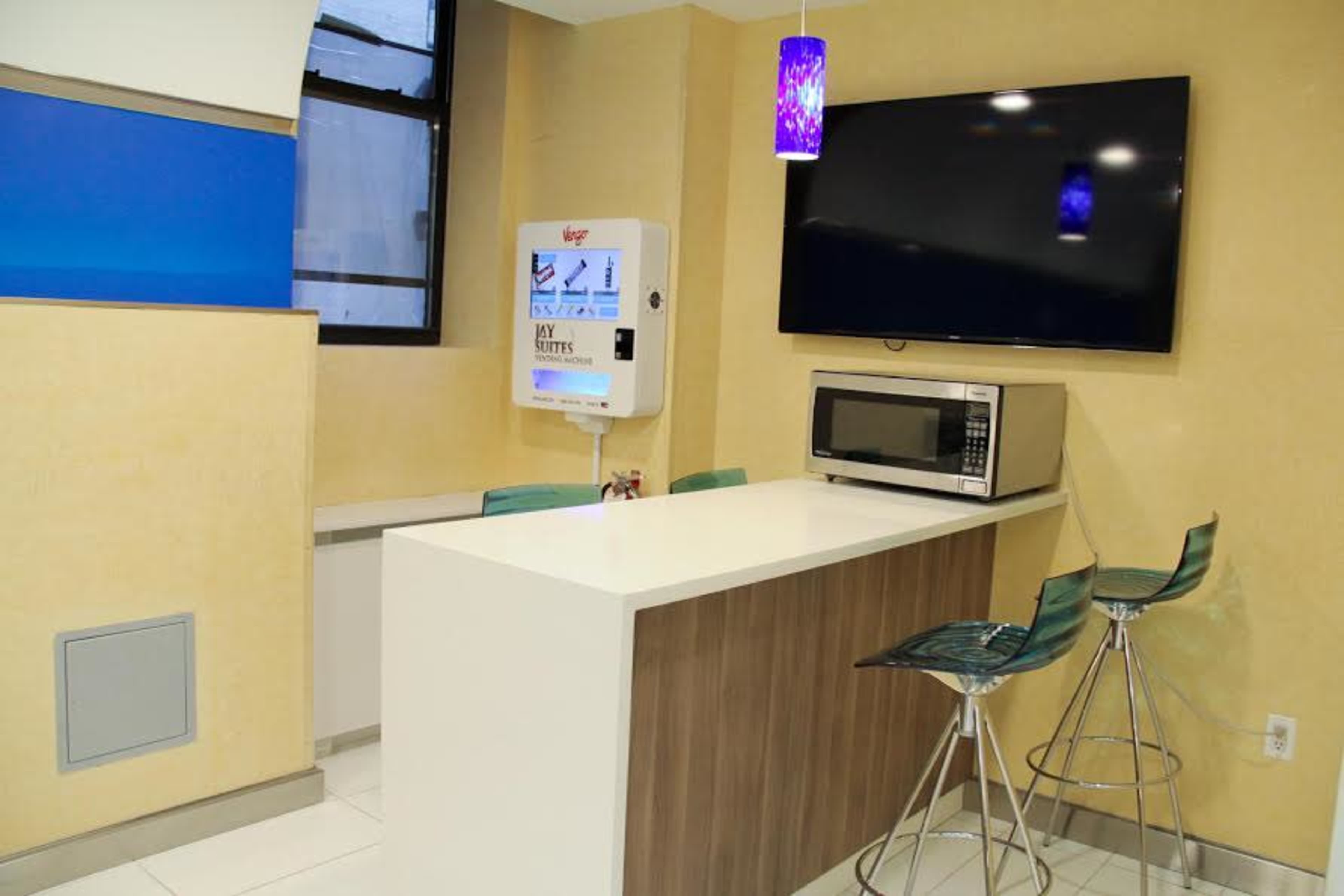 A modern kitchen area with a countertop, bar stools, a microwave, and a wall-mounted television.