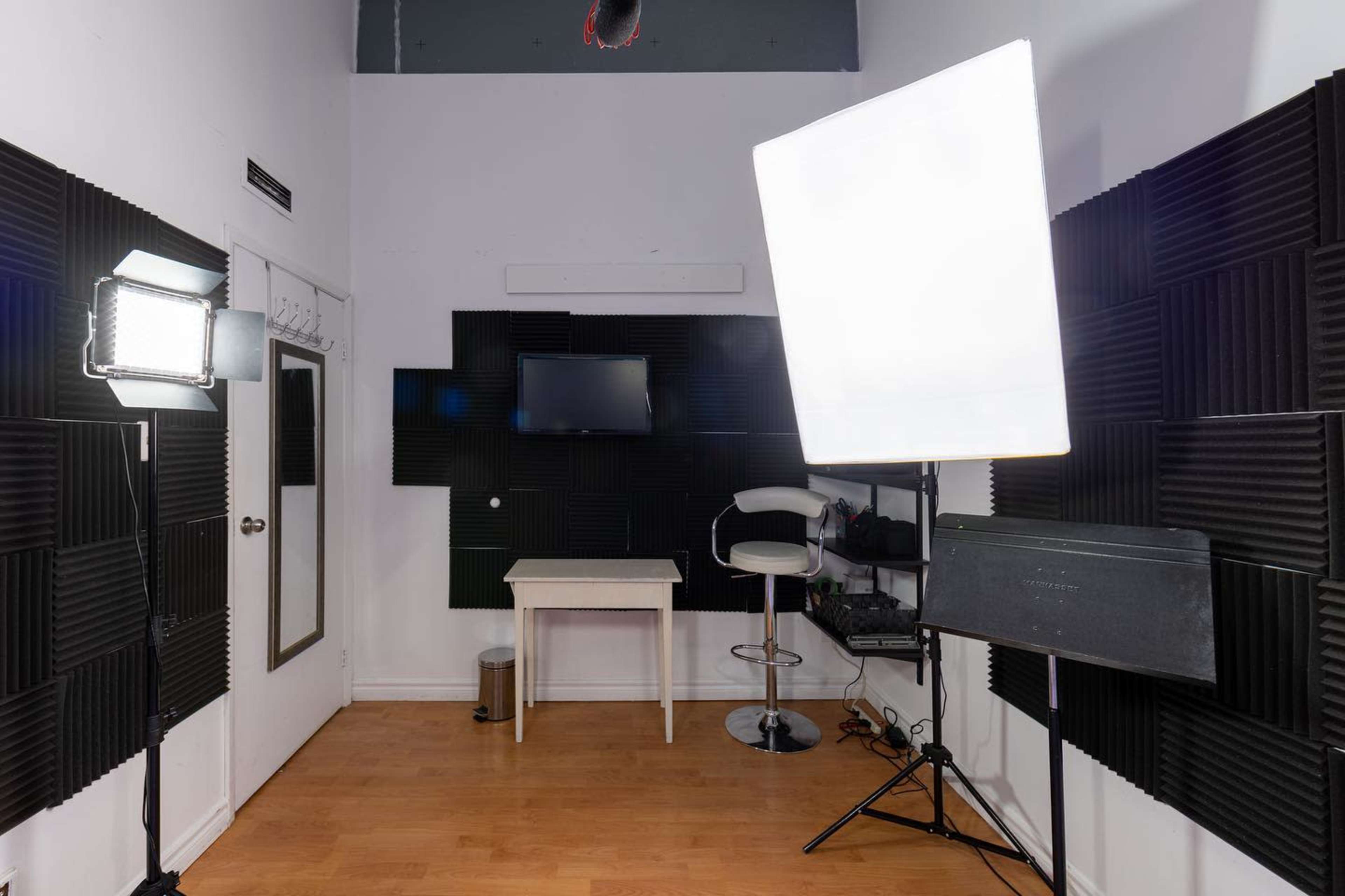 A small studio space equipped with acoustic panels, a television, a table, and various lighting equipment.