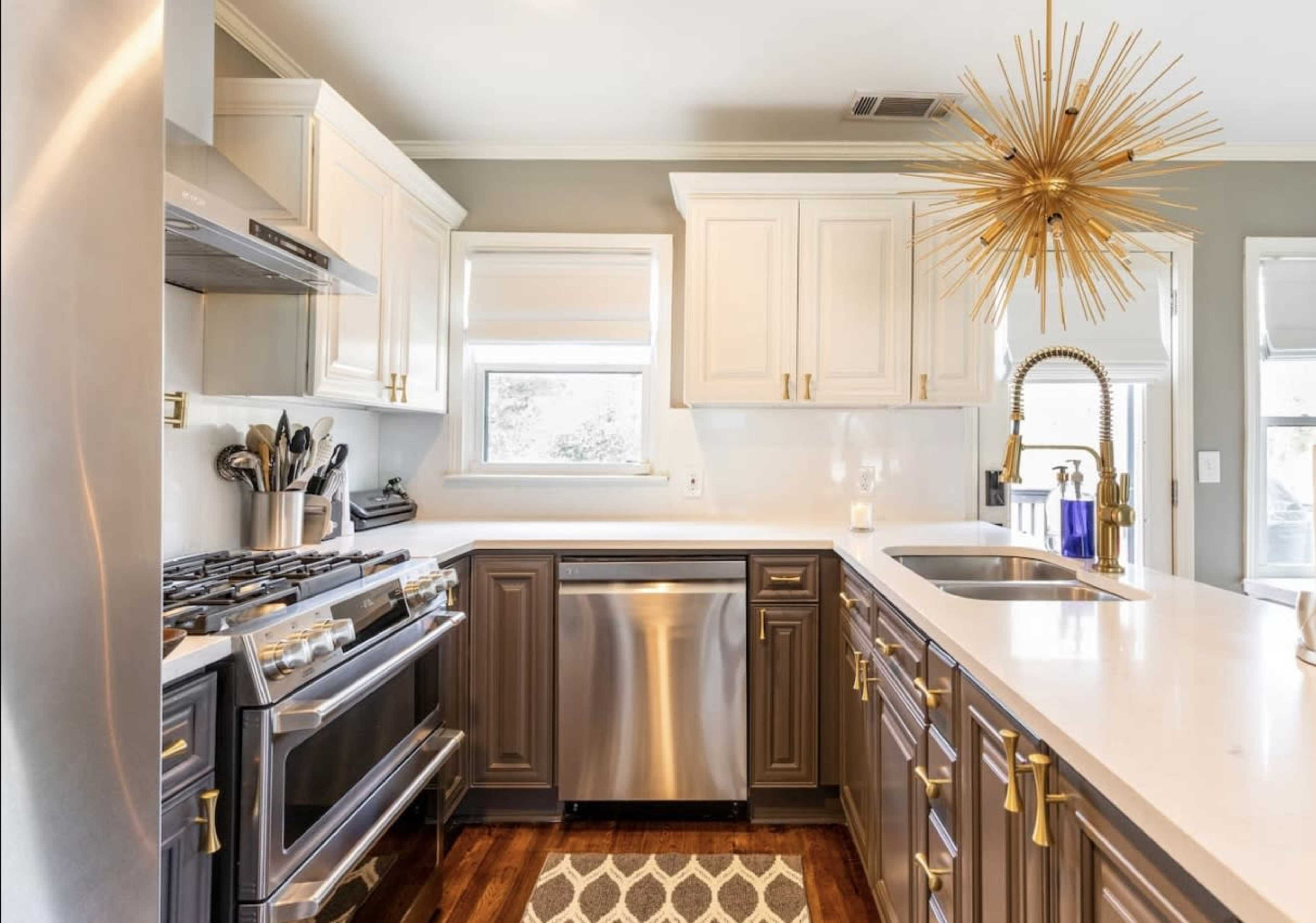 A modern kitchen features a stainless steel gas range, dishwasher, and a golden starburst pendant light above a white countertop.