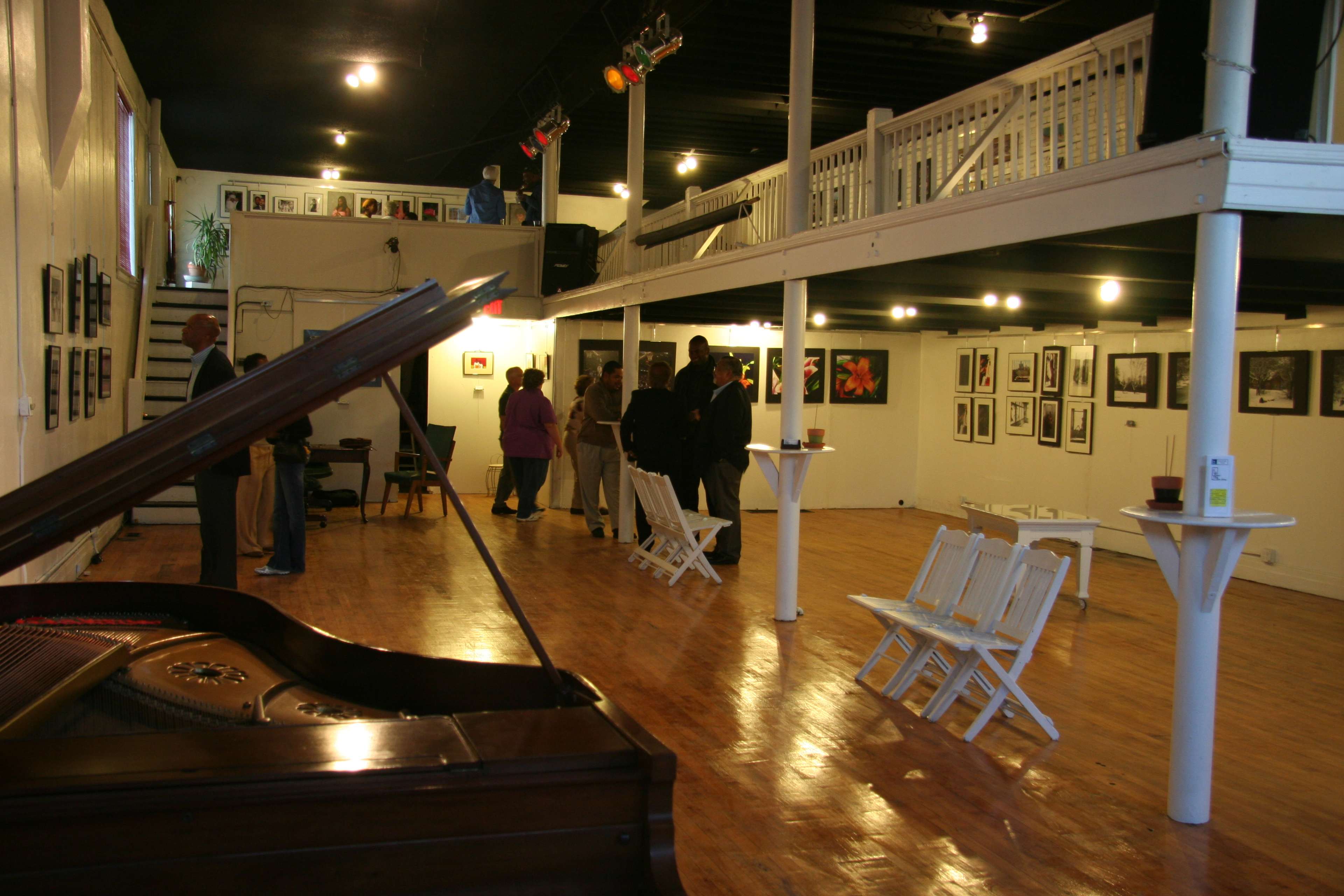 An art gallery with a grand piano in the foreground and visitors engaging with the displayed photographs on the walls.