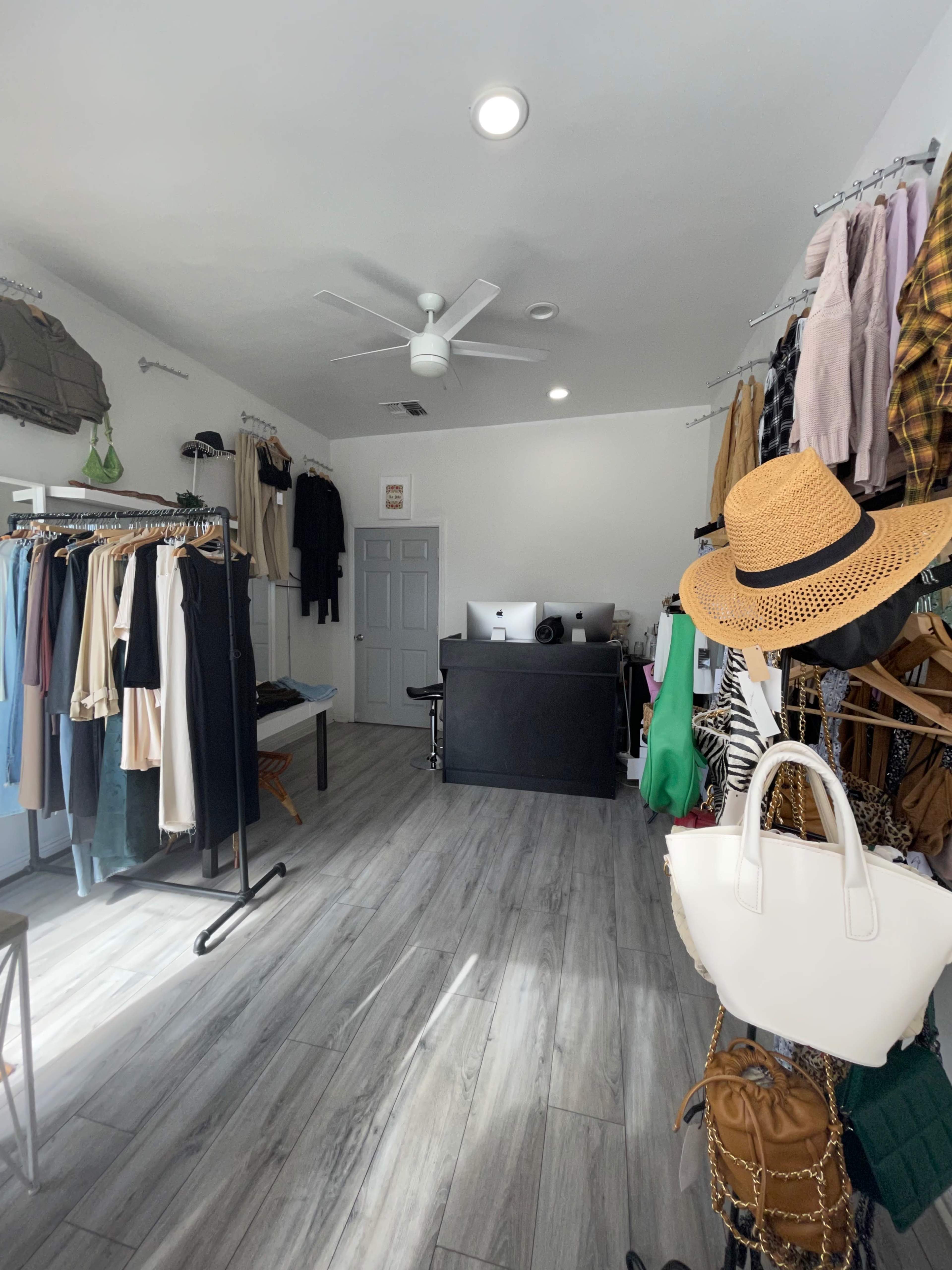A clothing boutique with racks of apparel on the left and hanging garments on the right, alongside a checkout counter at the back.
