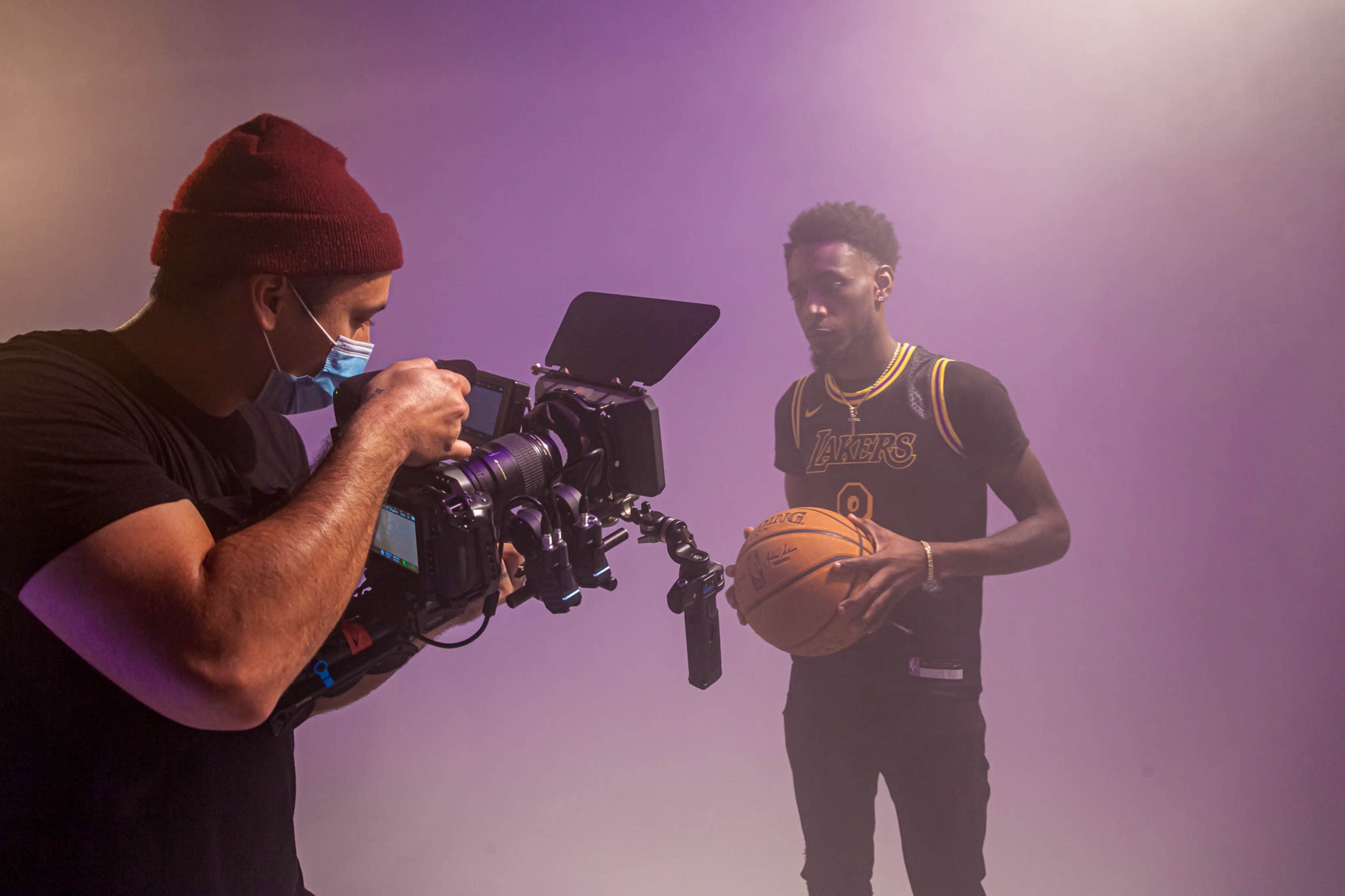 A photographer captures a basketball player holding a ball while posing in a studio with purple lighting.