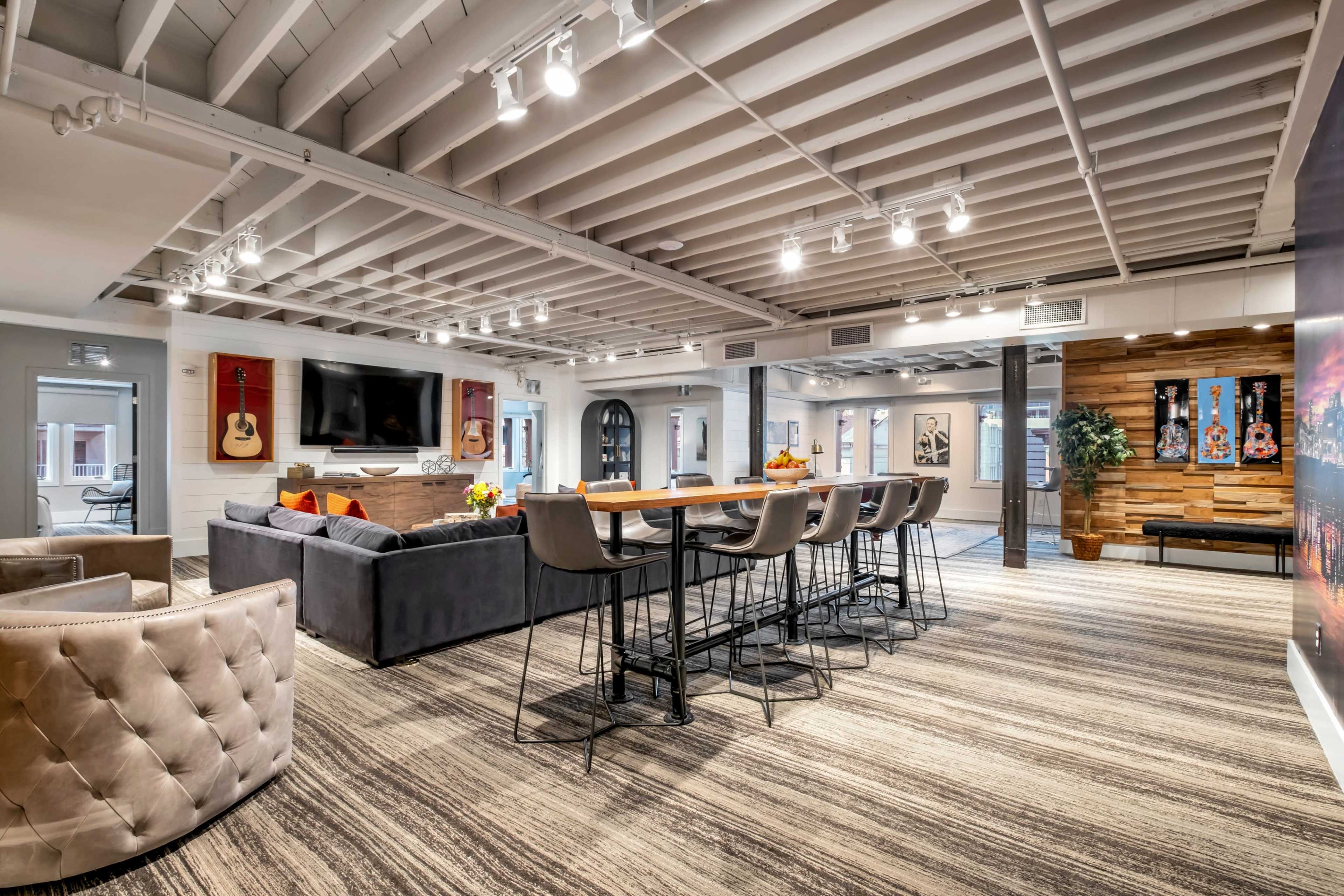 The image shows a modern, open-concept lounge area with a seating space, a long dining table, and various decorative elements.