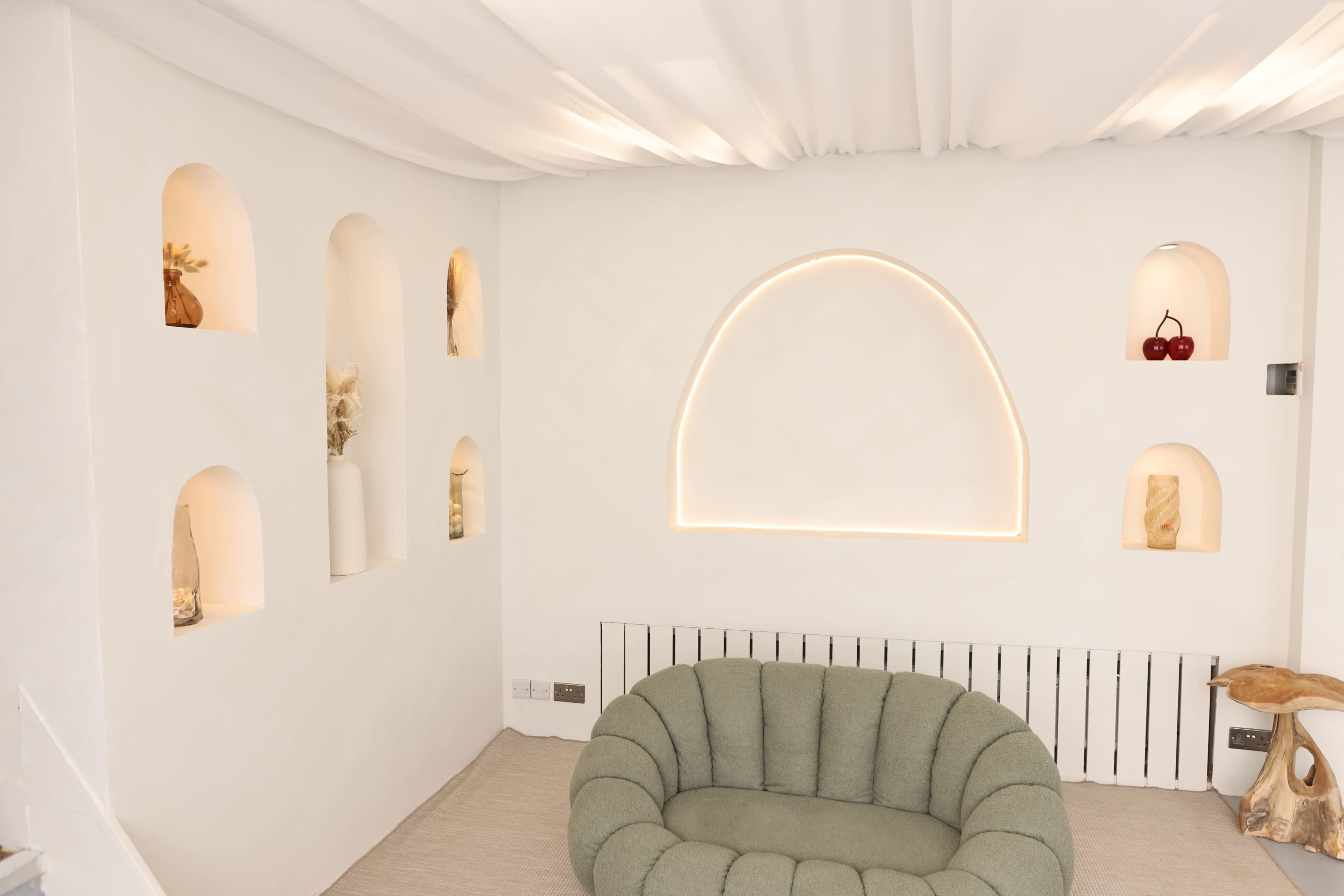 The image shows a minimalist interior with a rounded green couch, illuminated alcoves displaying decor, and a softly lit arch in the wall.