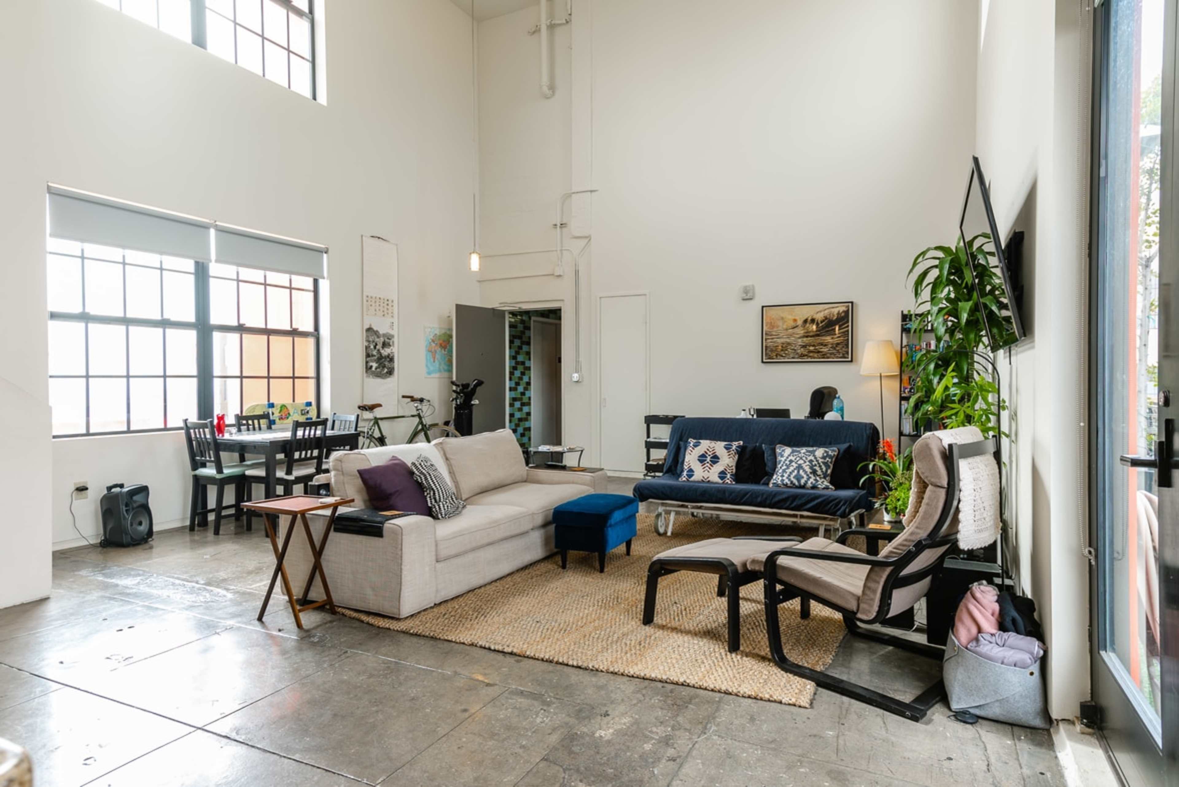A spacious living area with a sofa, armchairs, a coffee table, and a dining table in a bright, well-lit room featuring large windows.