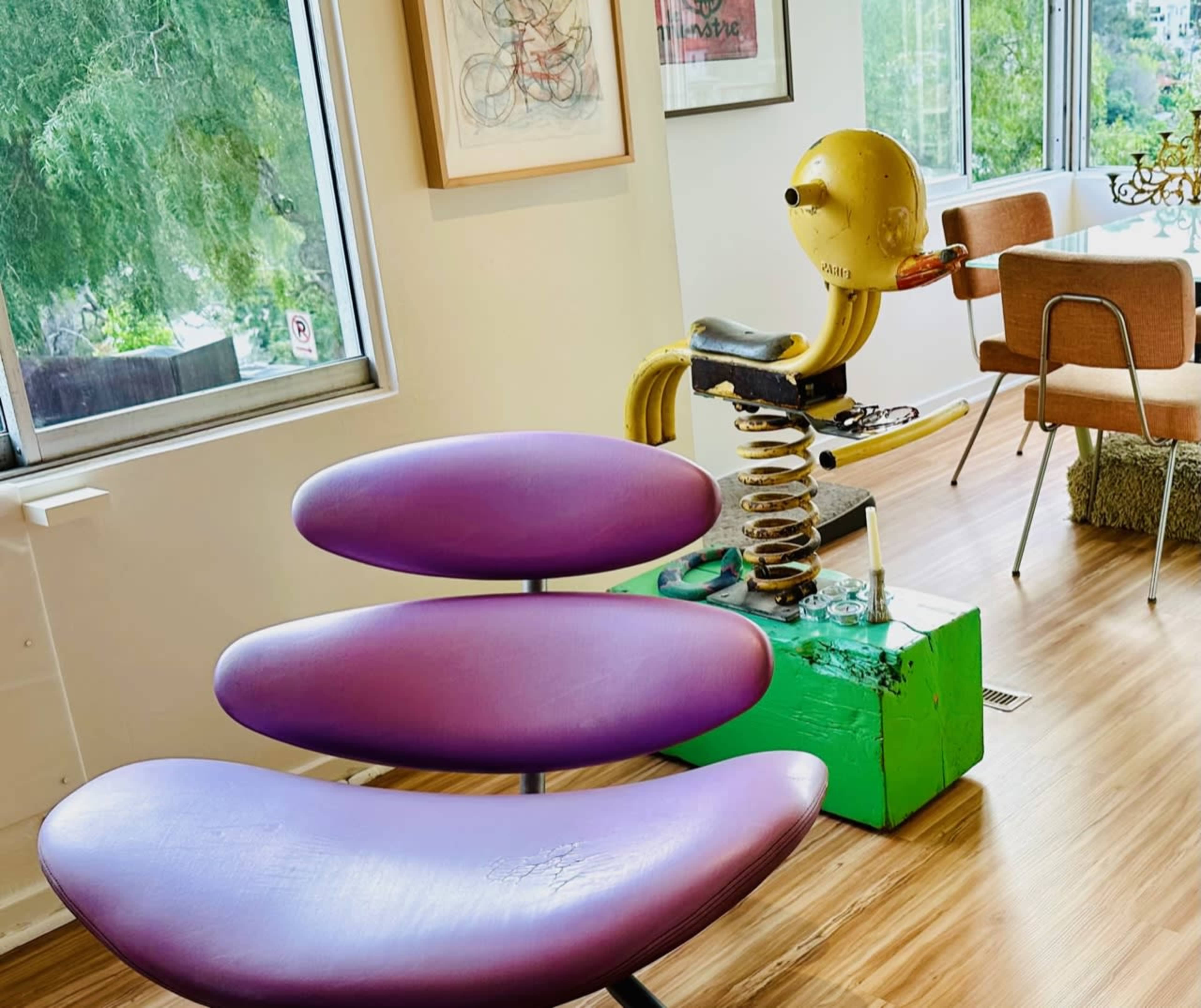 The image shows a modern interior with a purple, three-section chair and a colorful, whimsical spring-mounted sculpture resembling a bird.