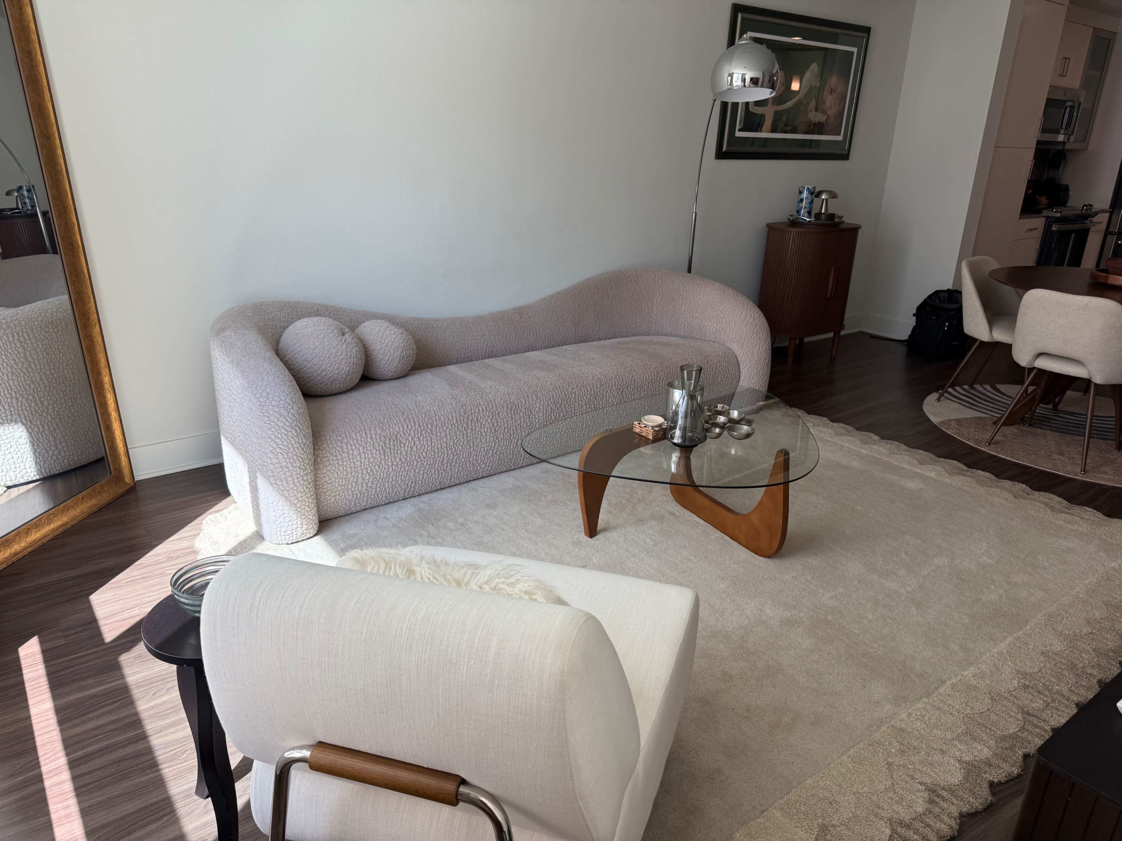 The image shows a modern living room with a pink curved sofa, a glass coffee table, and an armchair on a light rug.