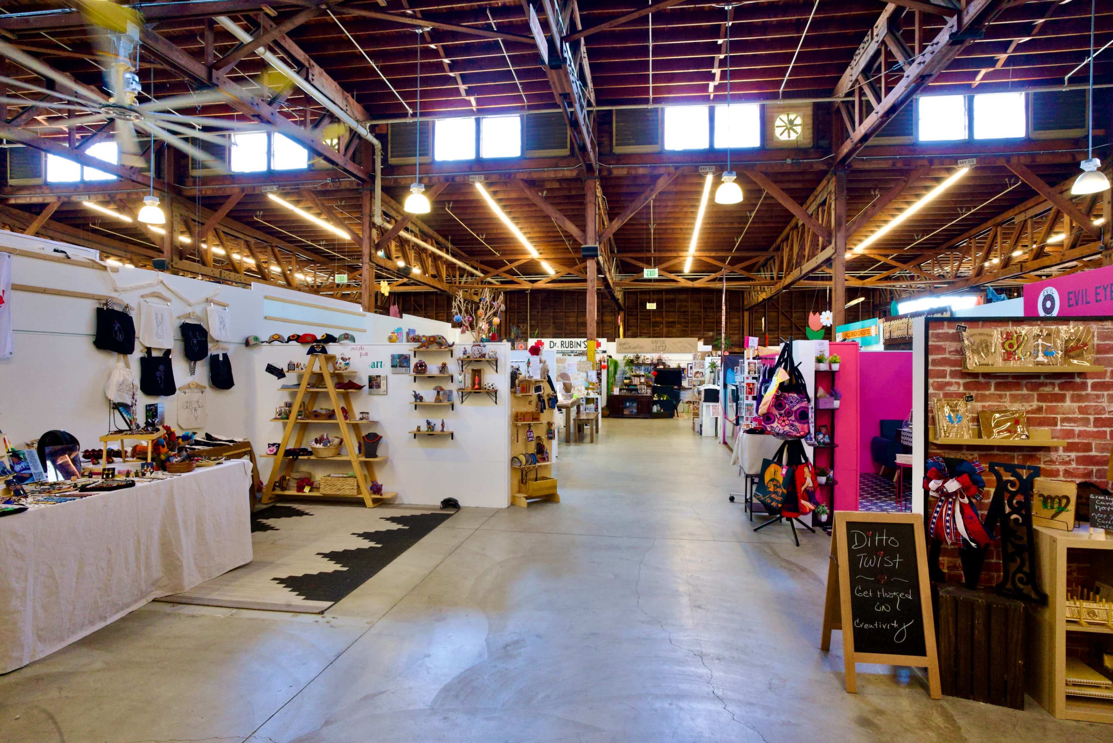 The image shows a spacious indoor market with vendors displaying various goods on tables and shelves, illuminated by overhead lights.