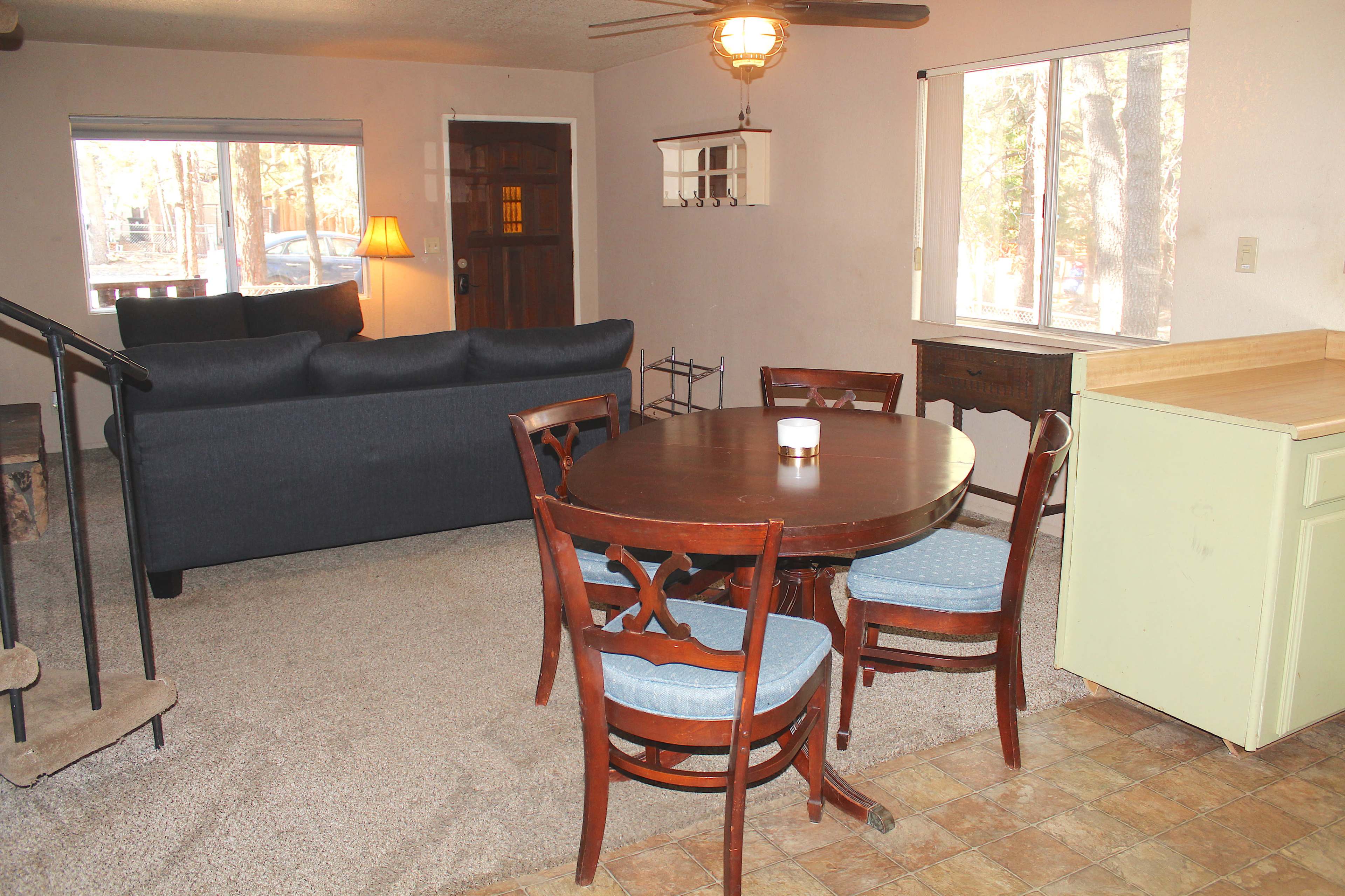 A living area featuring a dark blue sofa, a round dining table with four chairs, and a window overlooking a natural setting.