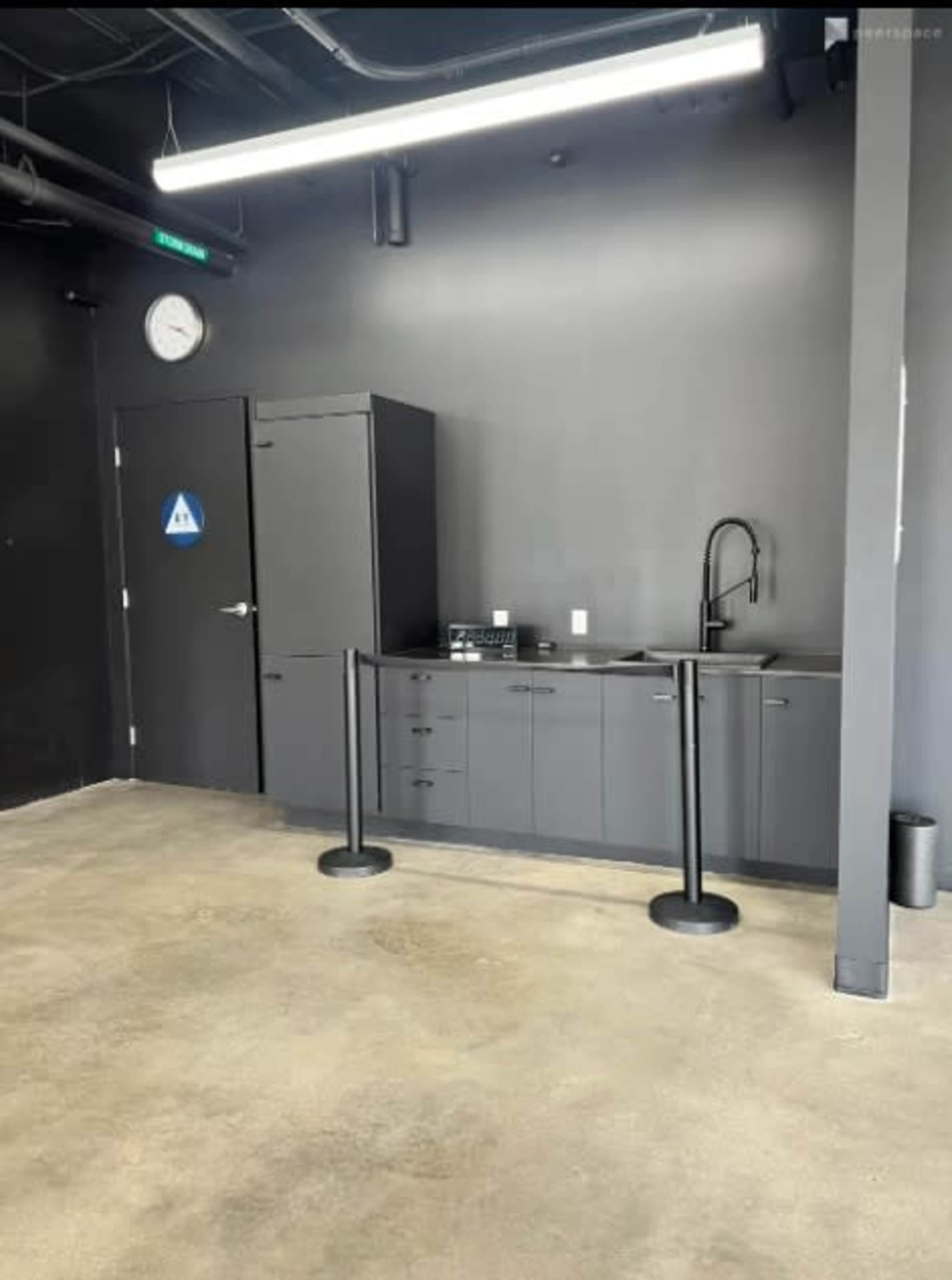 A dark-walled room with a gray cabinet, a sink, and a bathroom sign on the door.