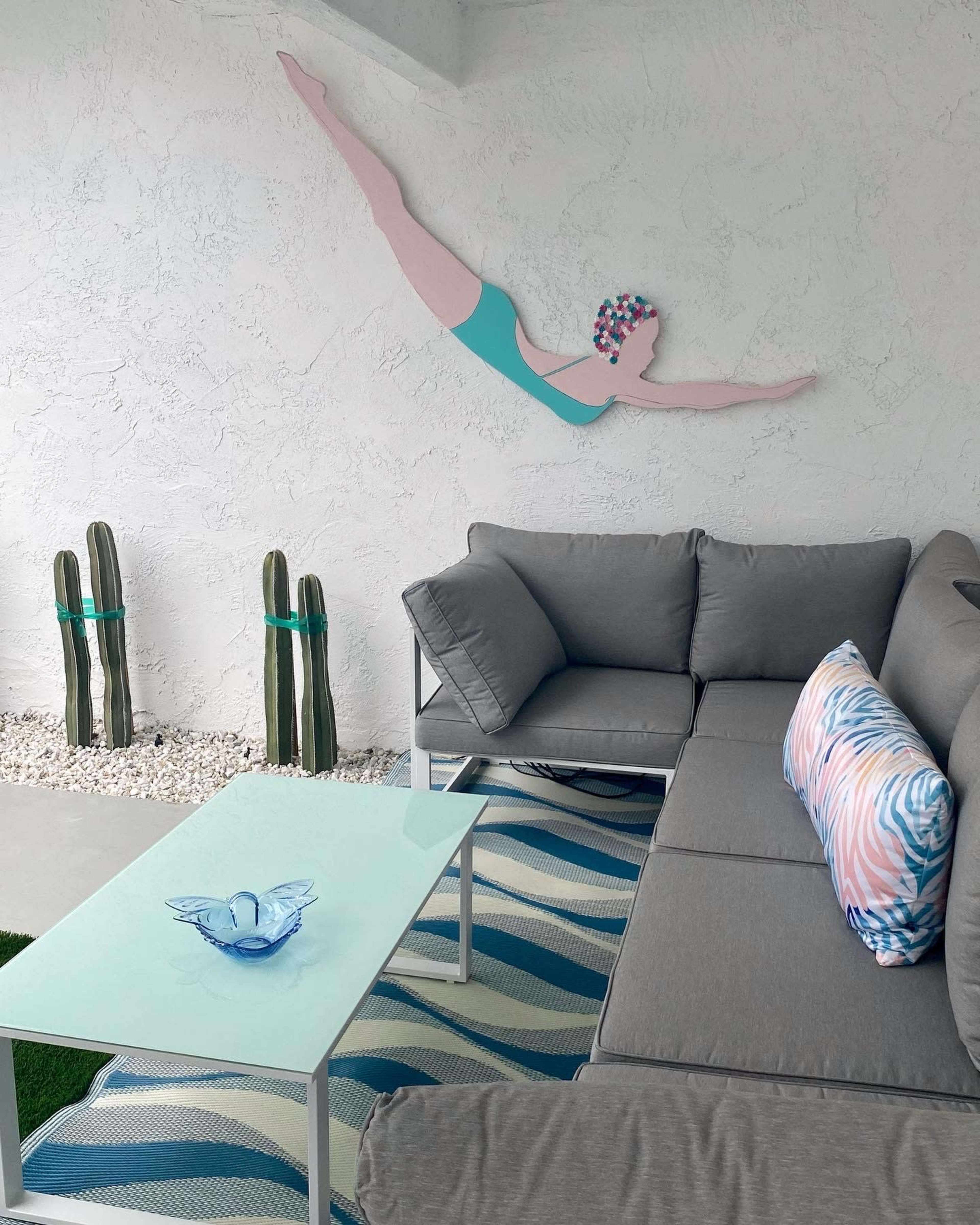 A modern outdoor seating area features gray sofas, a light blue table, and a wall art piece depicting a swimmer.