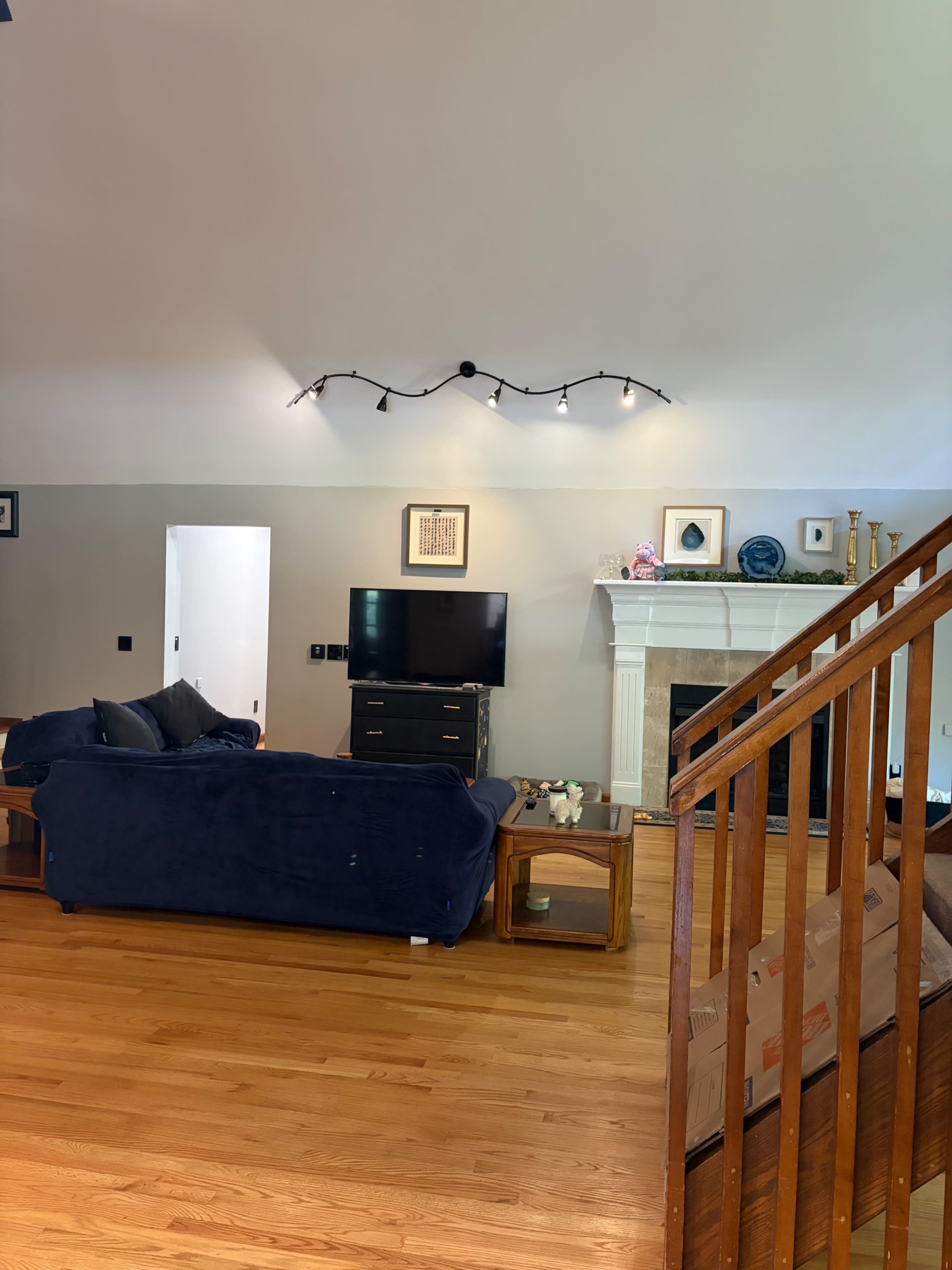 The image shows a living room with a blue couch, a television on a stand, a fireplace, and wooden stairs leading to an upper level.