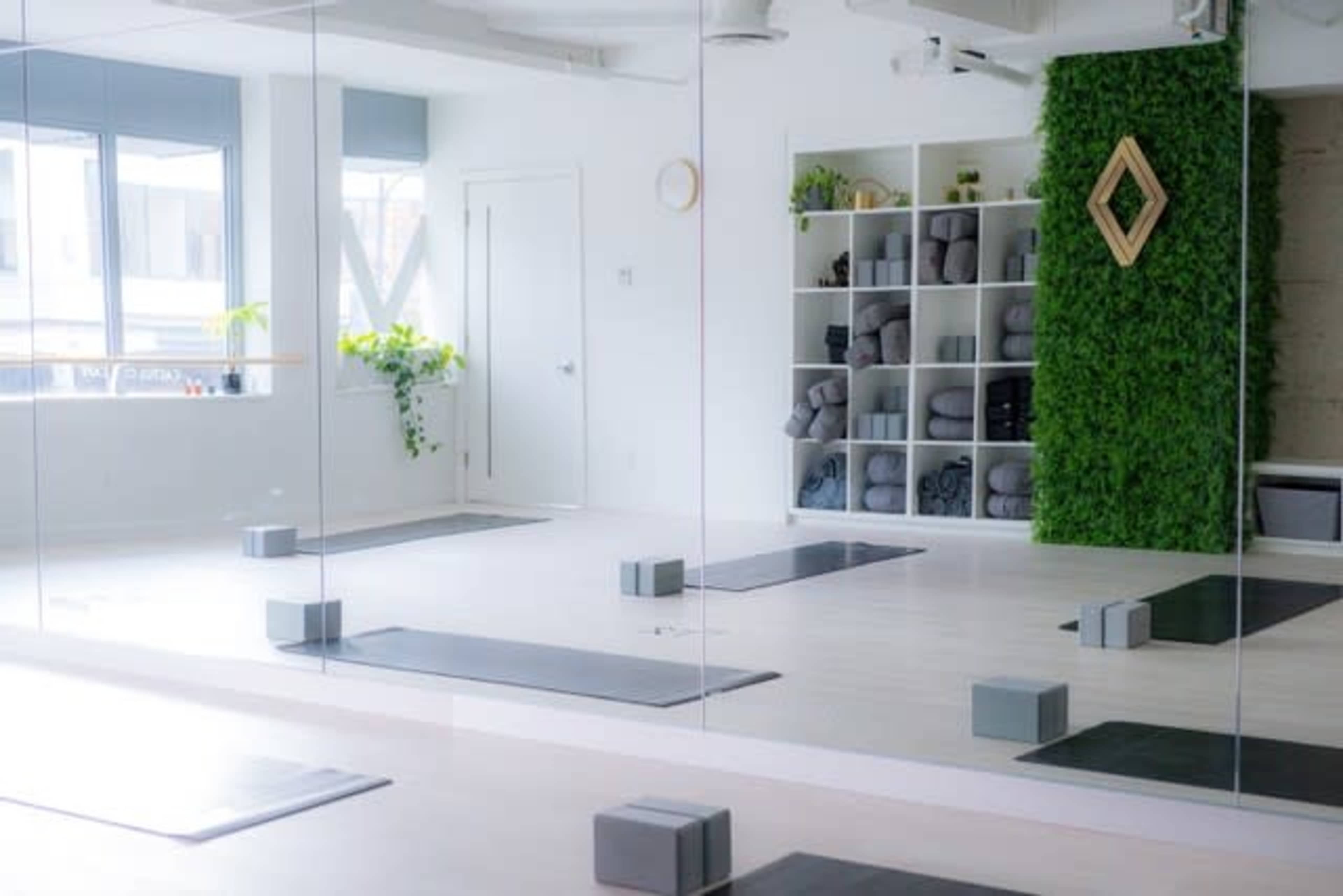 The image shows a yoga studio with mirrored walls, yoga mats, blocks, and green wall decor.