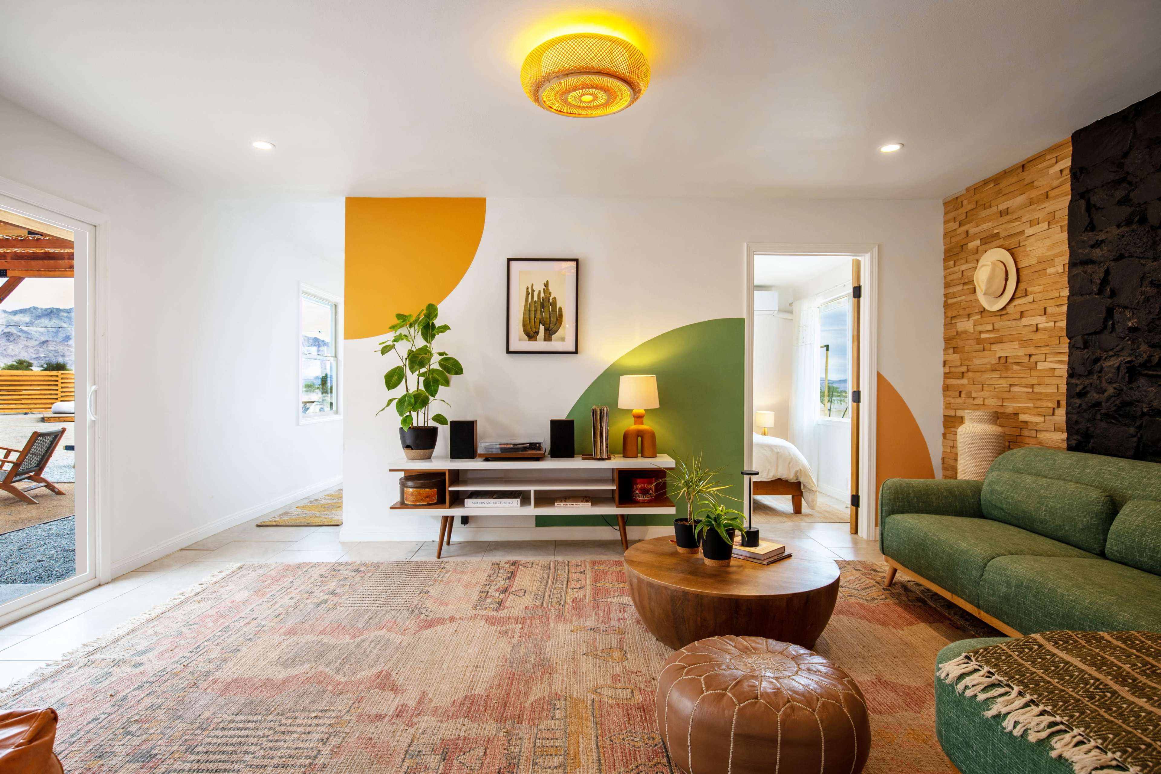 The image shows a modern living room with a green sofa, a wooden coffee table, and walls featuring a combination of yellow and green shapes along with natural wood accents.