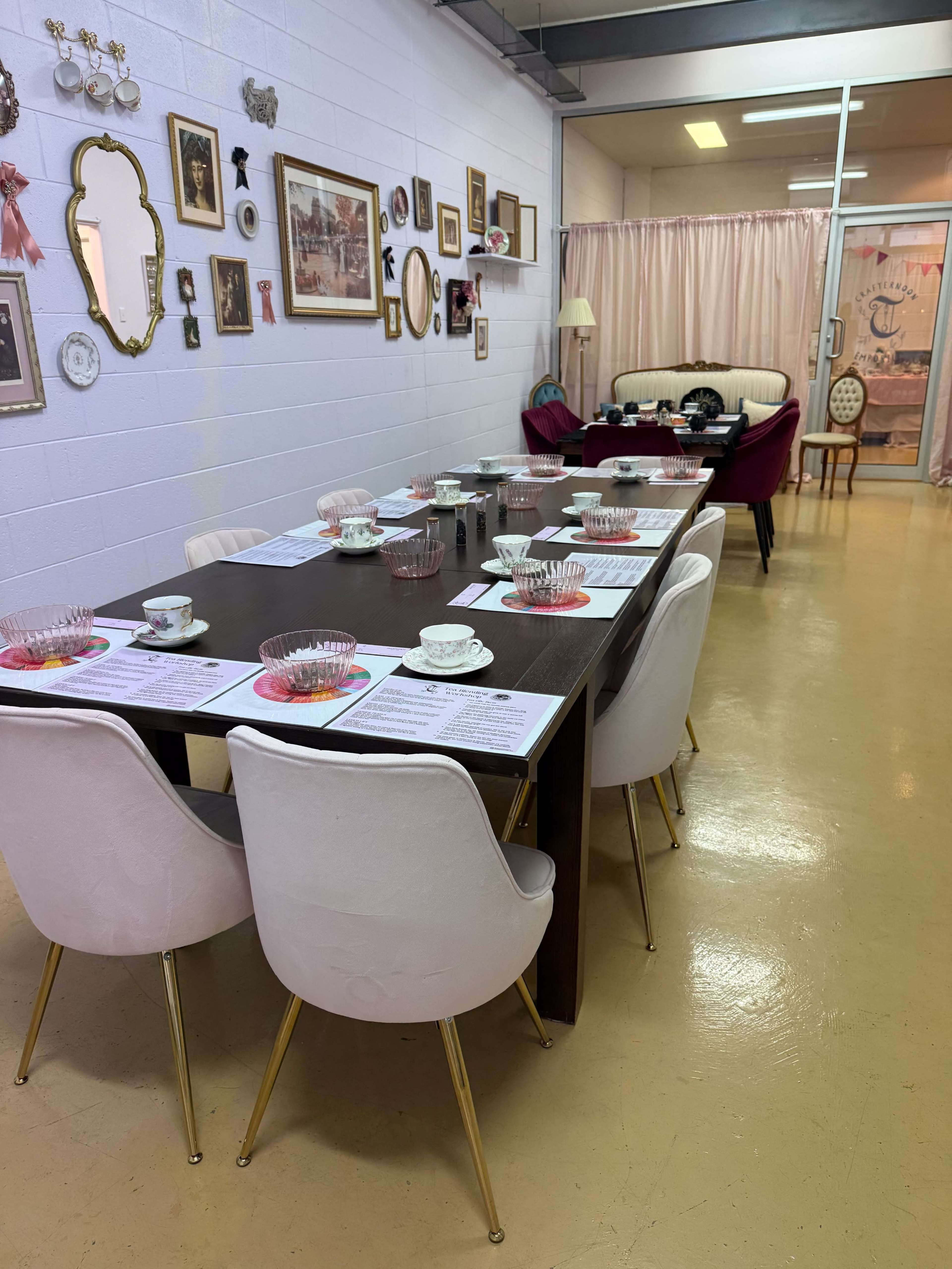 The image shows a dining area with a long table set for a meal, surrounded by white chairs, and decorated with various framed pictures on the walls.