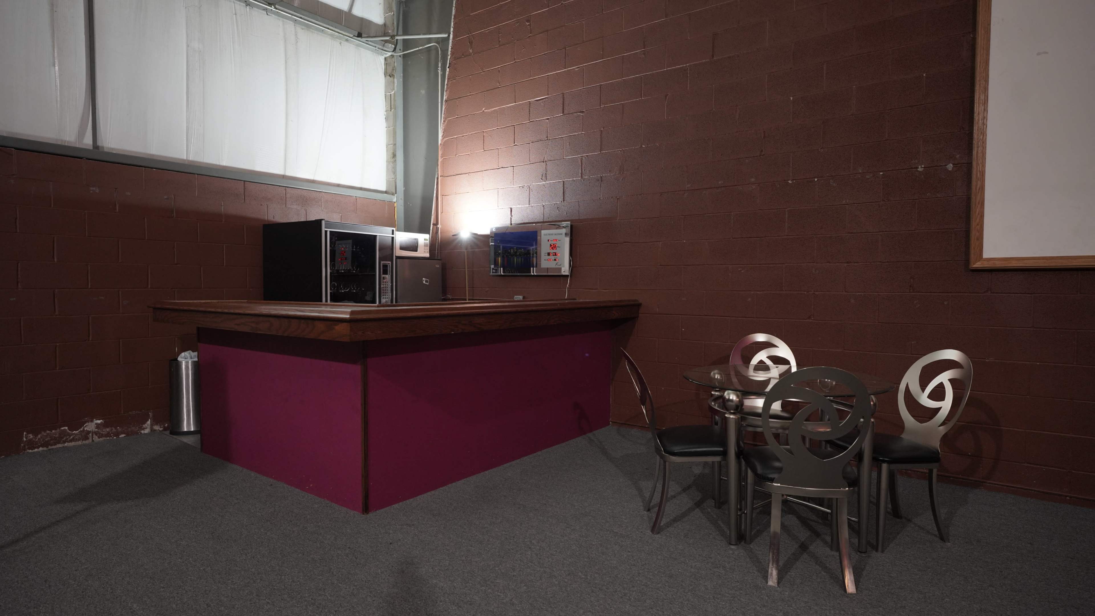 A small area with a purple counter, a microwave, and a round table with four chairs against a brown brick wall.